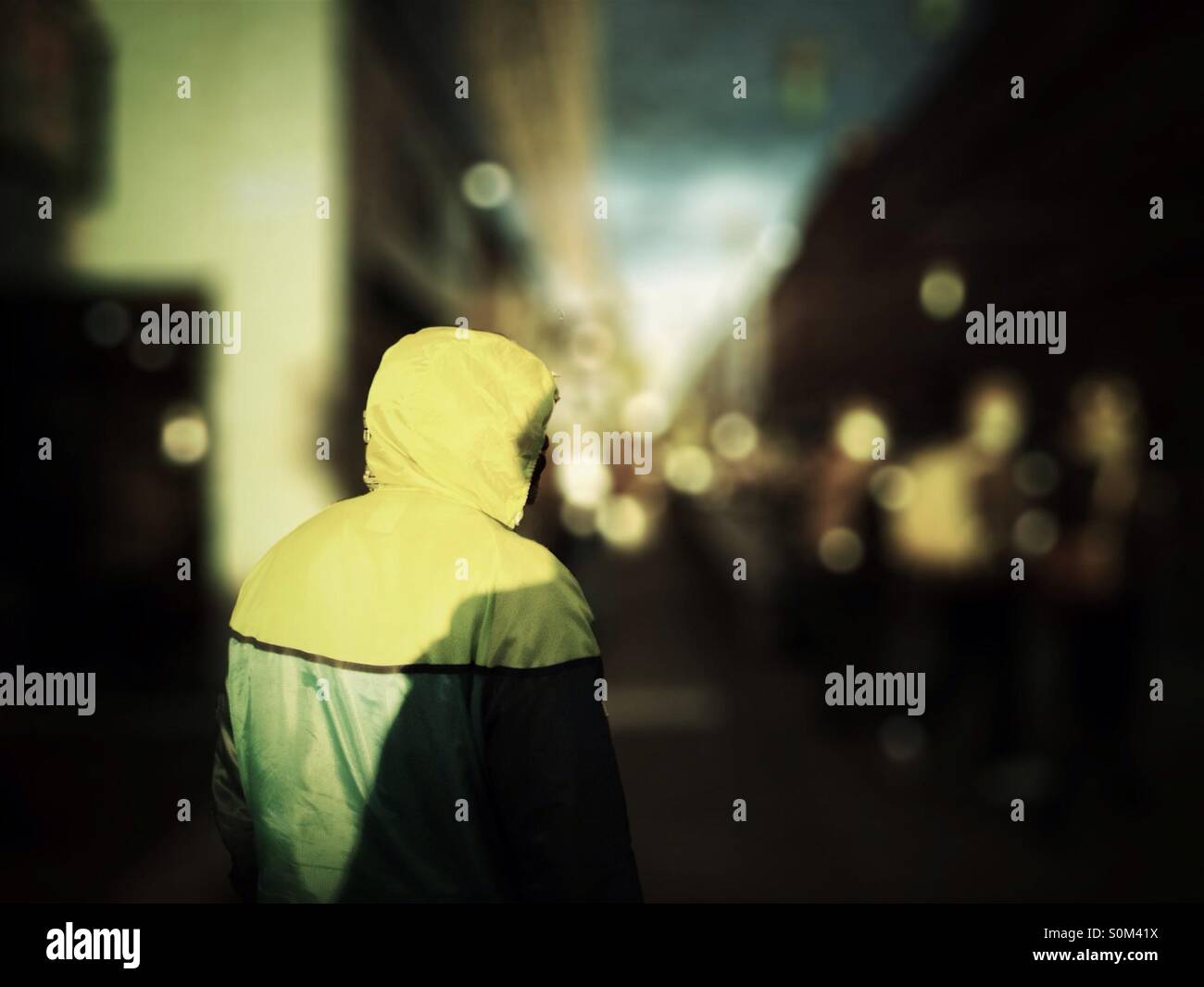 L'homme en jaune et vert veste pluie spirts en face de flou artistique flou d'urban street - Image de stock capturée avec un smartphone