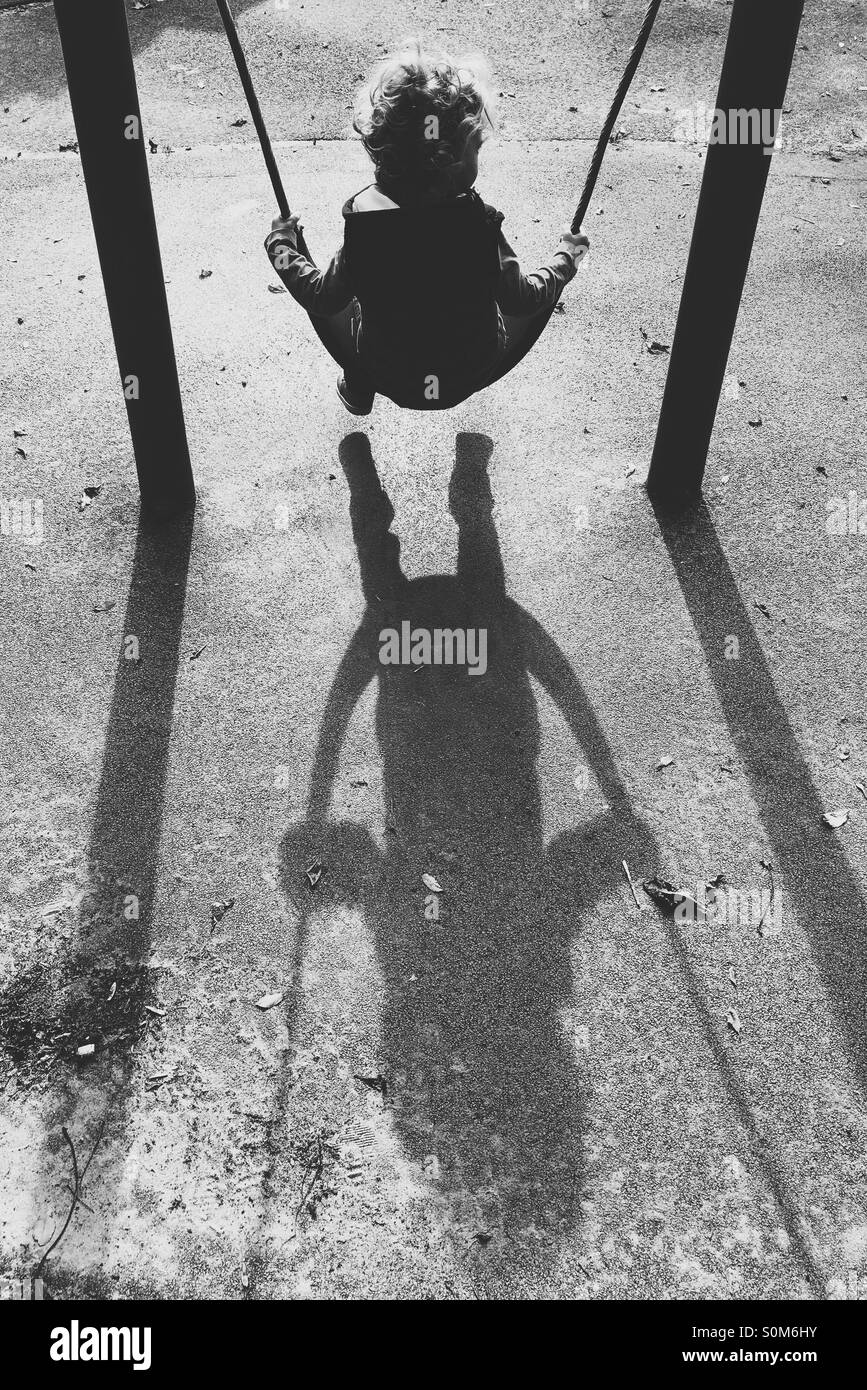 Garçon sur swing avec de longues ombres Banque D'Images
