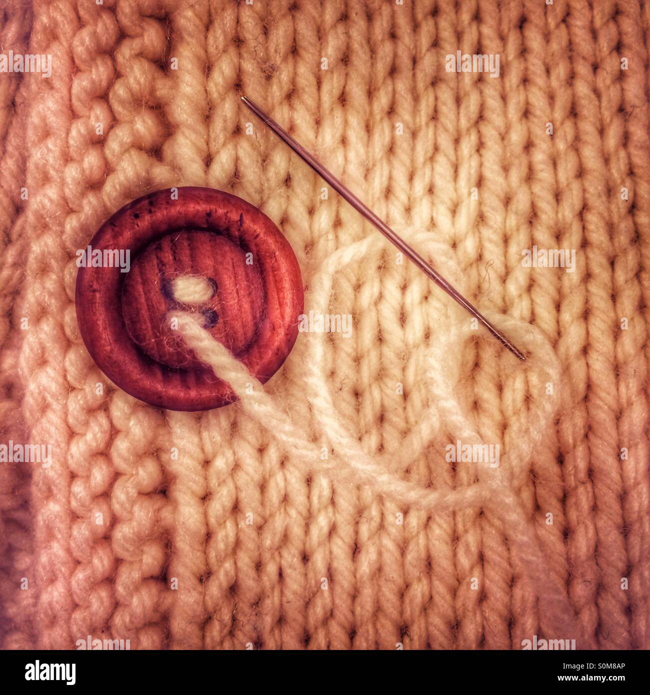 La couture d'un bouton d'une main veste en tricot Banque D'Images