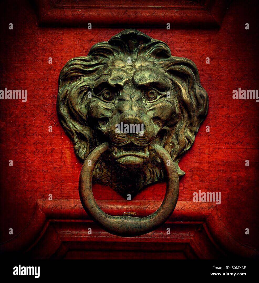 Un heurtoir en laiton vert de gris d'une tête de lion sur une porte rouge. - Image de stock capturée avec un smartphone
