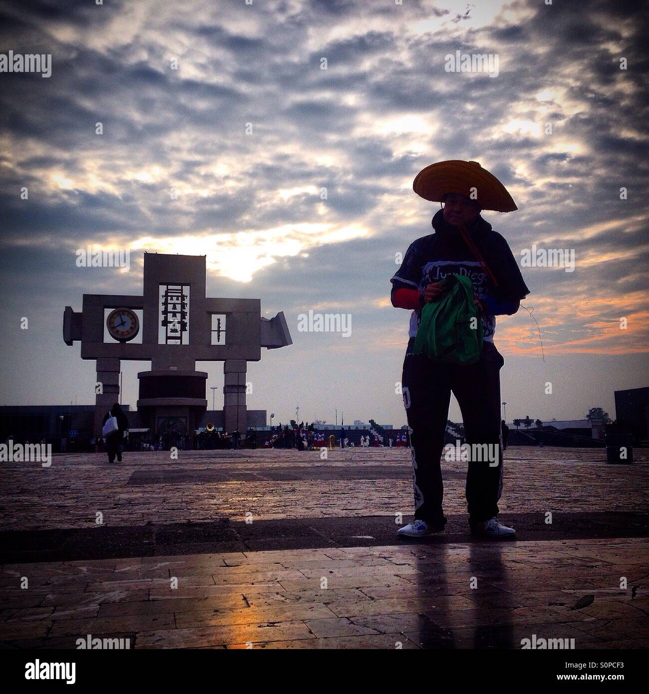 La silhouette d'un homme portant un chapeau mexicain se trouve en face de la croix de la basilique au cours du pèlerinage de Notre Dame de Guadalupe à Mexico, Mexique. - Image de stock capturée avec un smartphone