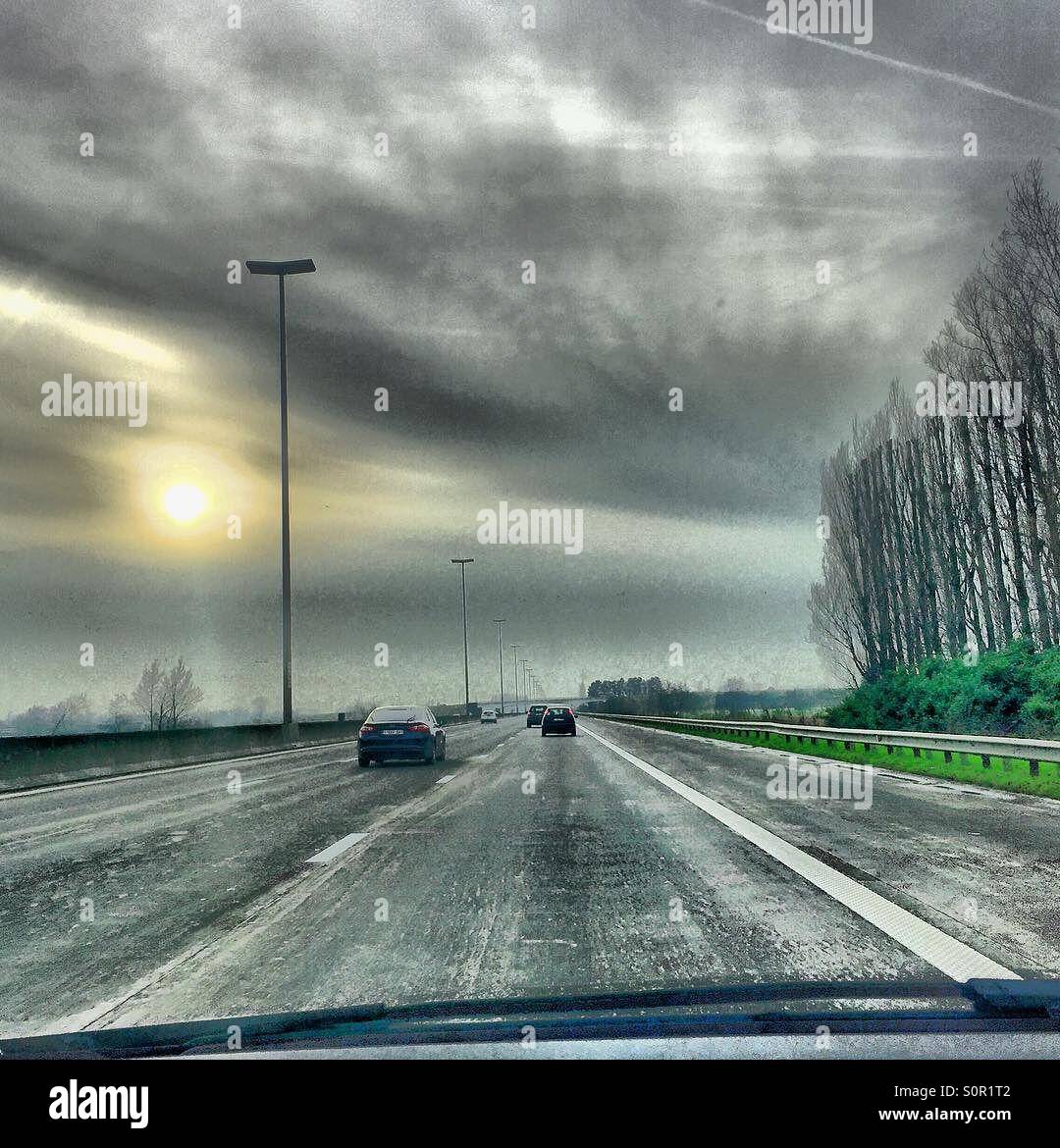 Soleil bas dans un ciel gris au-dessus d'une autoroute tranquille avec des peupliers, vu depuis la voiture - Image de stock capturée avec un smartphone