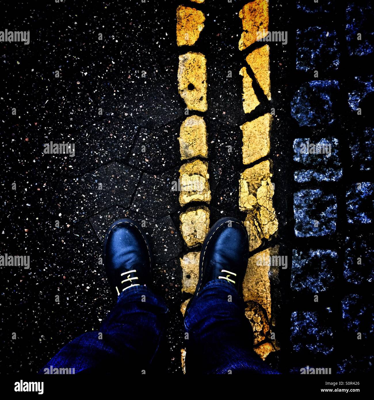 Pieds wearing blue Dr Marten bottes sur route avec lignes jaunes - Image de stock capturée avec un smartphone