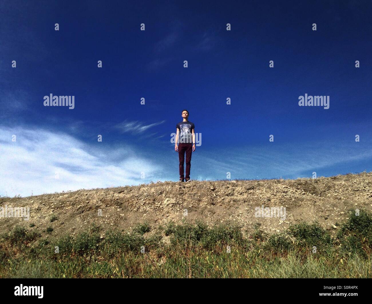 Un homme en t-shirt et pantalon brun se dresse sur une colline d'un plan commun sur le fond bleu ciel clair Banque D'Images