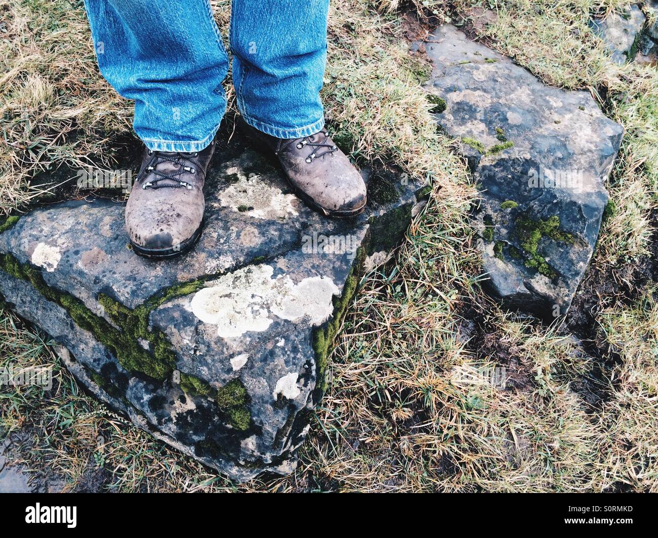 Les pieds d'un homme en jeans et des bottes de randonnée, debout sur un rocher au Royaume-Uni., de Teesdale Banque D'Images