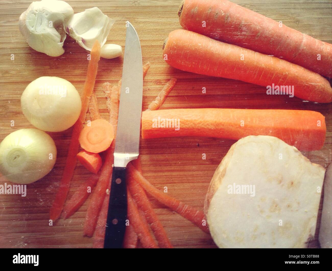 Différents légumes-racines (oignon, carotte, céleri-rave) et un couteau sur une planche à découper en préparation pour la cuisson Banque D'Images