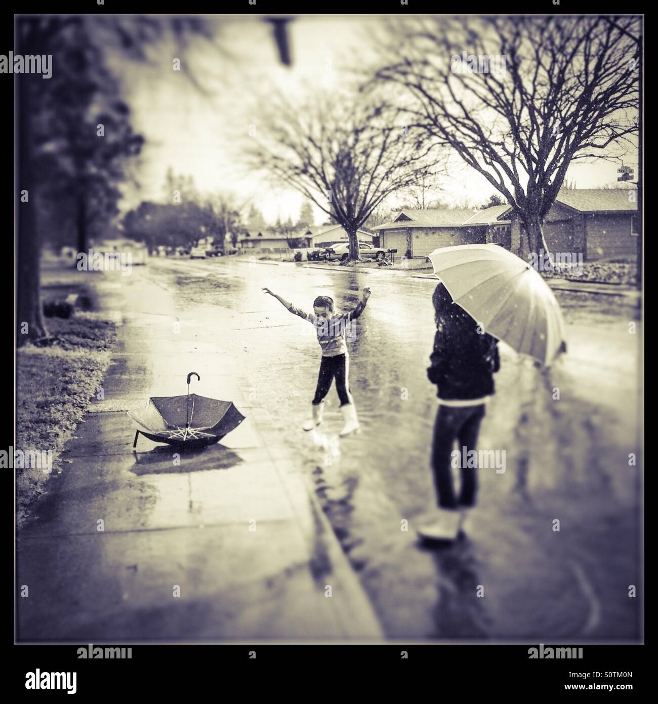 Une jeune fille de 12 ans et son frère de 7 ans jouer dehors sous la pluie. Banque D'Images