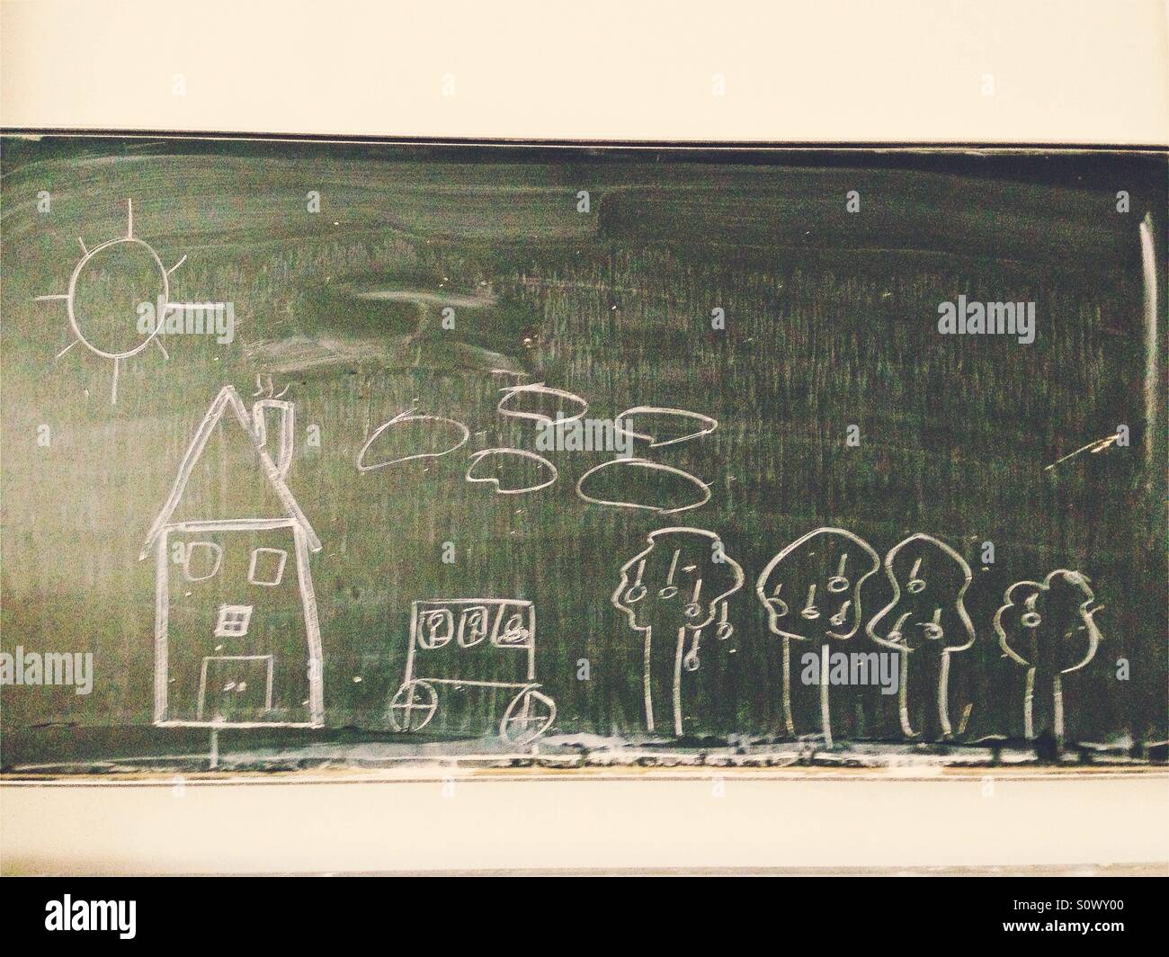 Une maison, une voiture, arbres et nuages dessiné à la craie blanche sur un tableau à l'école verte - Image de stock capturée avec un smartphone