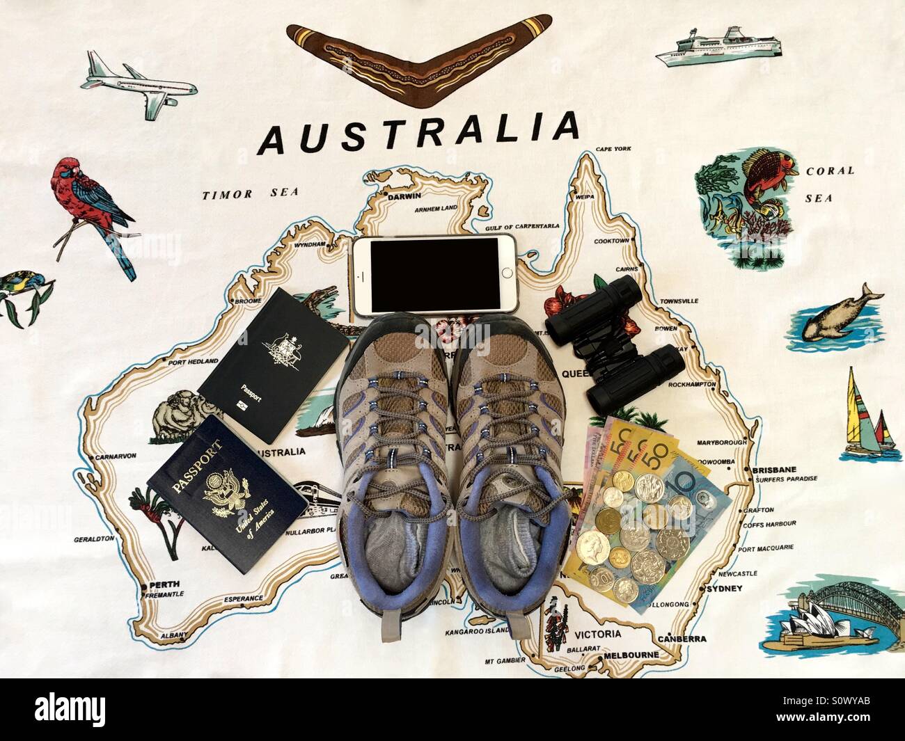 Une paire de bottes de randonnée pour les femmes, les passeports, les jumelles, smartphone et monnaie australienne à l'intérieur d'une carte de l'Australie Banque D'Images