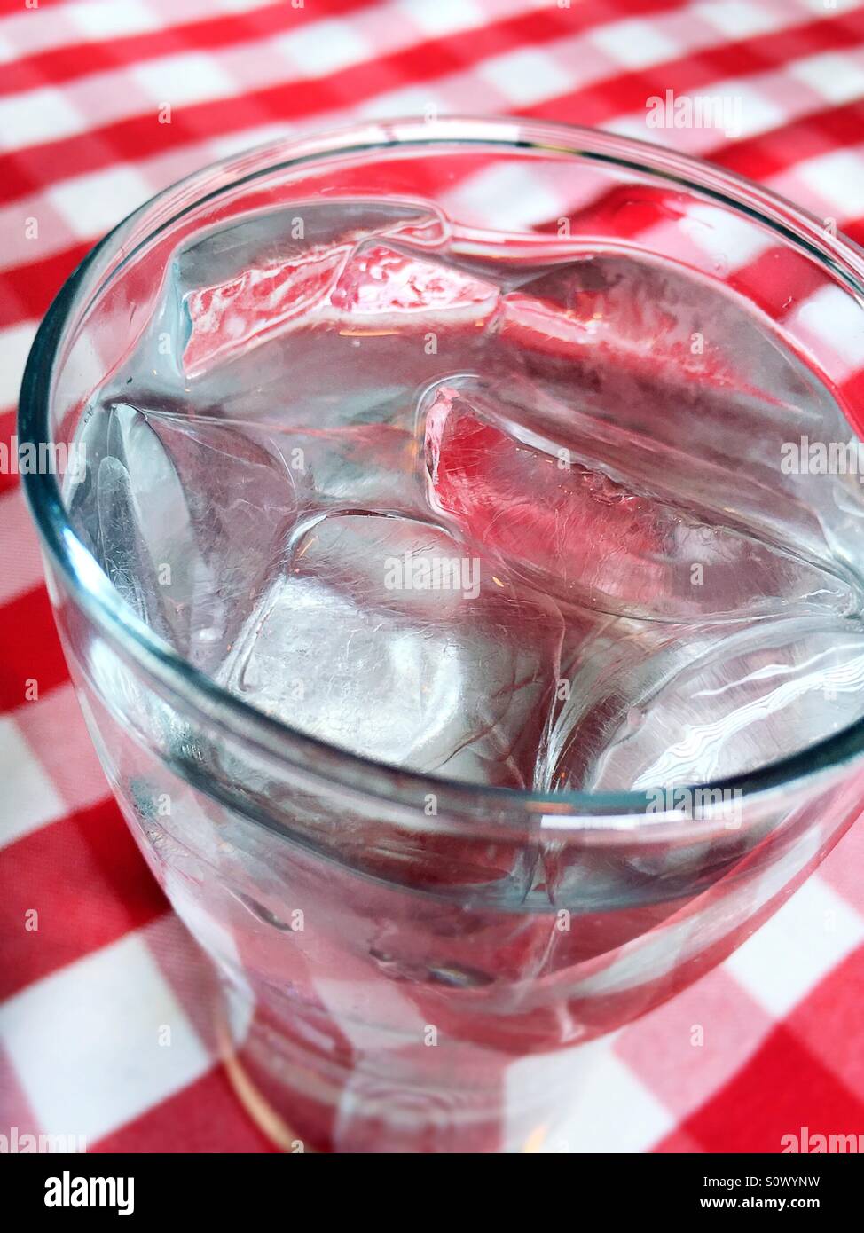L'eau de glace dans un verre transparent sur une nappe à carreaux rouges et blancs. - Image de stock capturée avec un smartphone