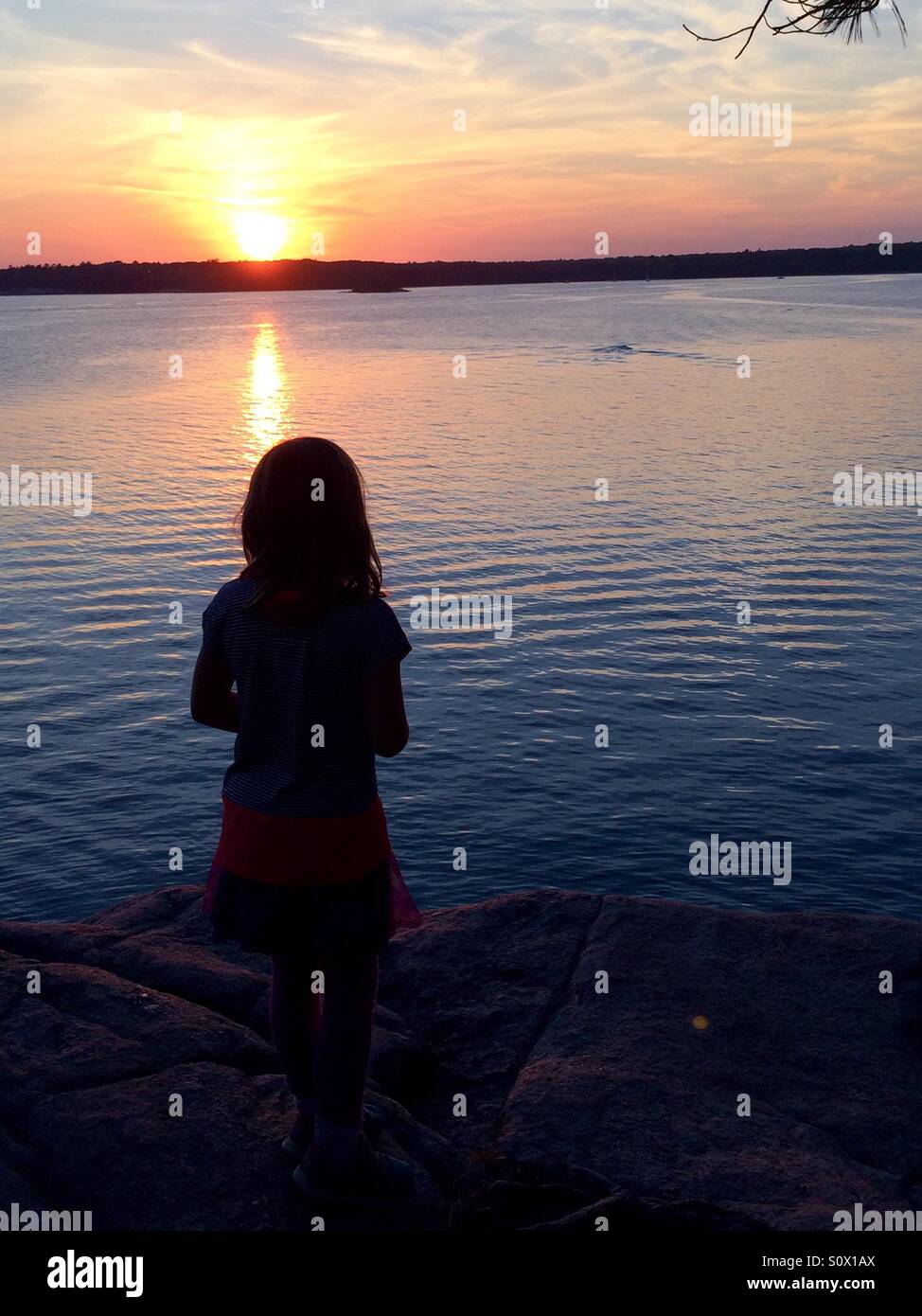 Silhouette de jeune fille au coucher du soleil en été sur un lac. Banque D'Images