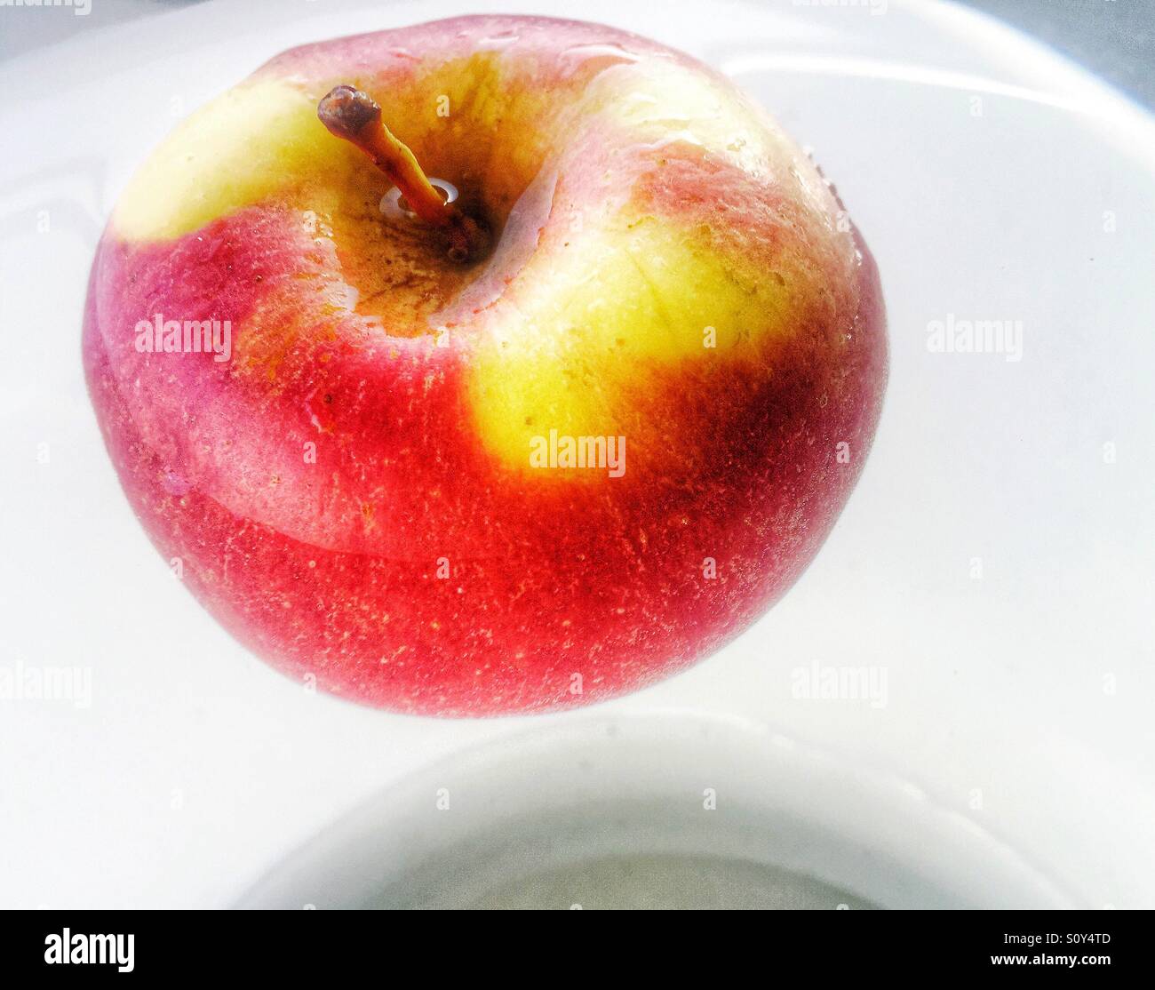 Une pomme rouge et jaune flottant dans un bol d'eau, moitié submergé. Banque D'Images