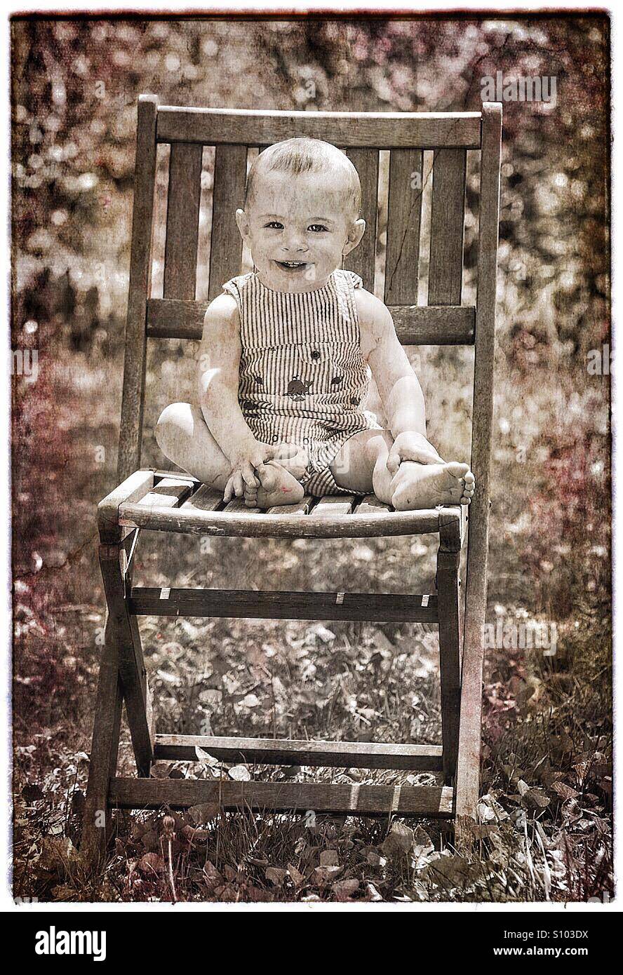 Bébé avec grand sourire assis sur une chaise à l'extérieur. Banque D'Images