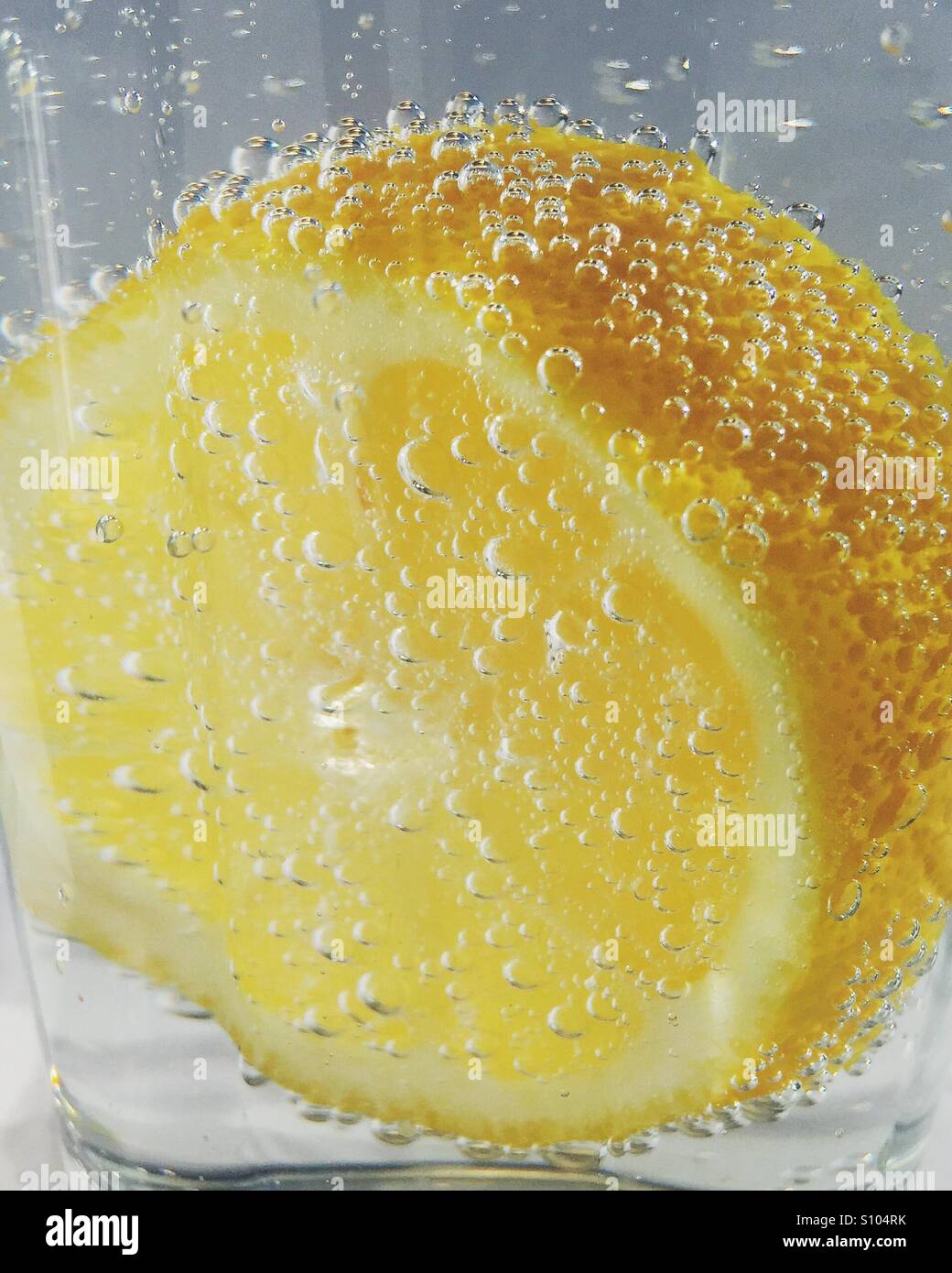 Vue rapprochée d'une tranche de citron au fond d'un verre d'eau gazeuse avec de petites bulles entourant le fruit - Image de stock capturée avec un smartphone