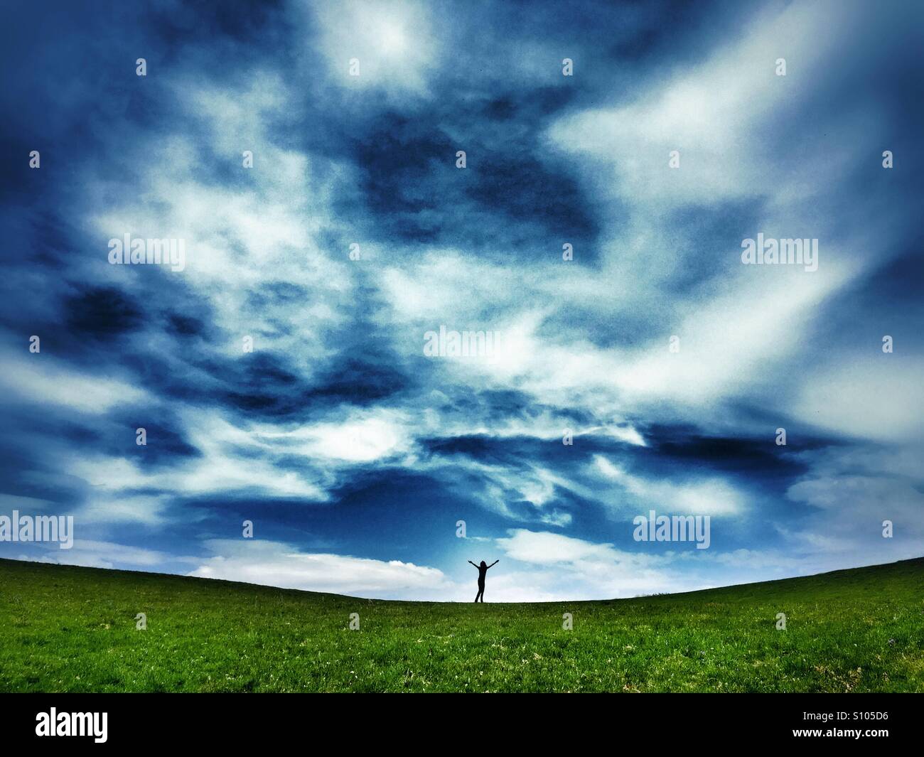 La figure lointaine avec les bras en haut de dip champ vert contre une blue cloudy sky - Image de stock capturée avec un smartphone