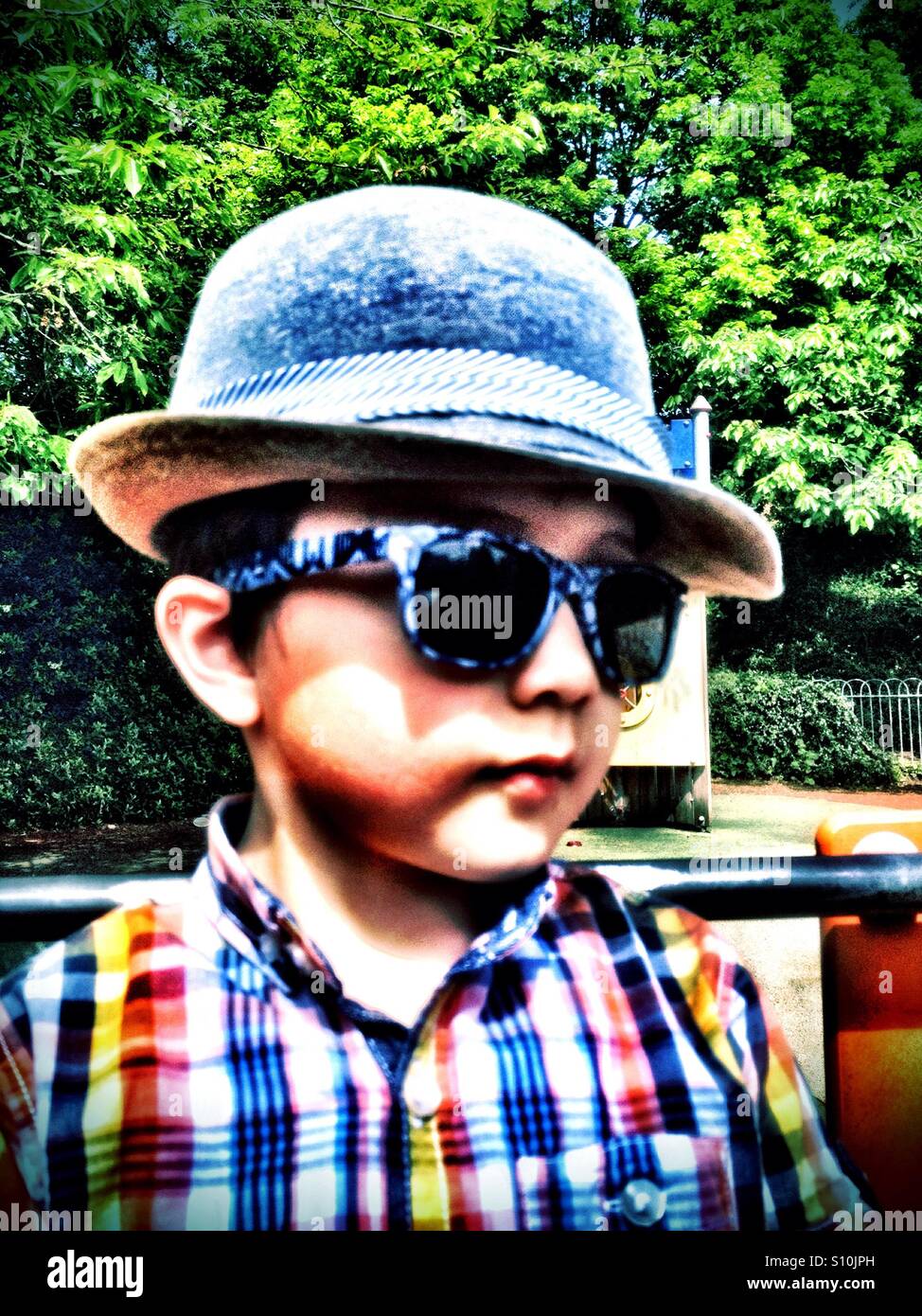 Un jeune garçon dans le parc portant chapeau et des lunettes de soleil. Banque D'Images
