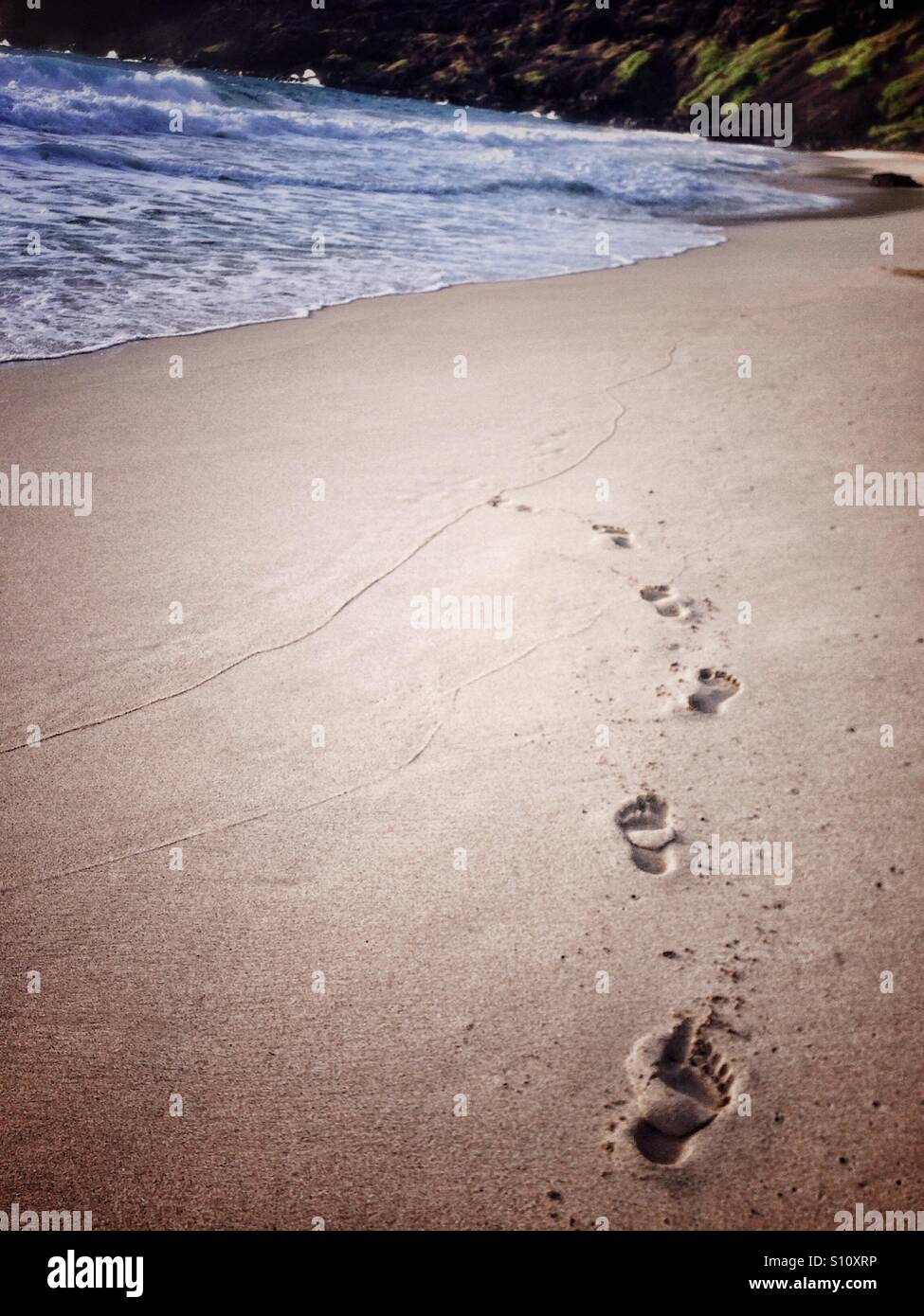 Footprints disparaissant dans l'eau sur la plage de Makapu'u, O'ahu, Hawaii. Banque D'Images