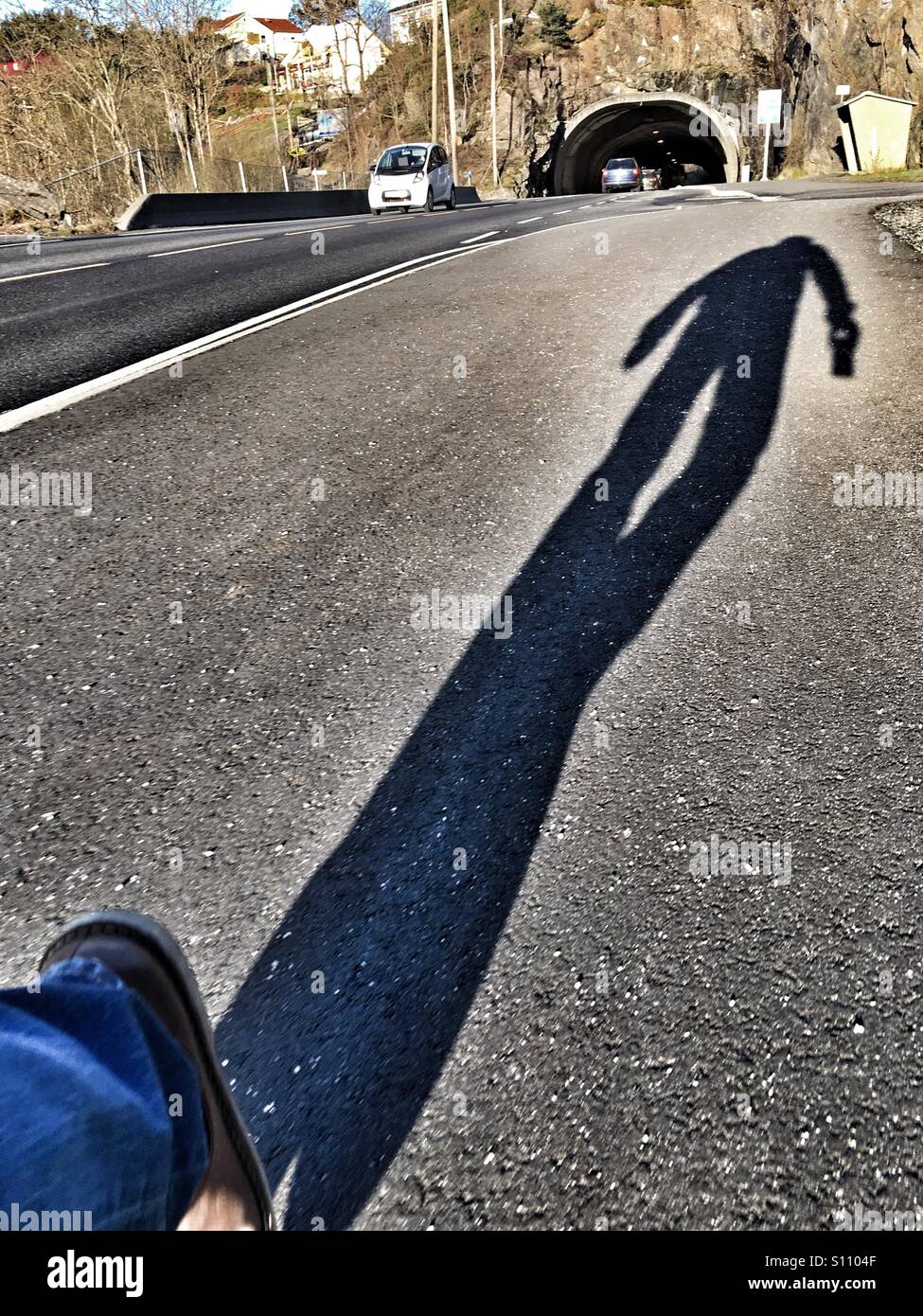 Ombre d'un homme marchant sur la chaussée en plus d'une route à chaussée unique Banque D'Images