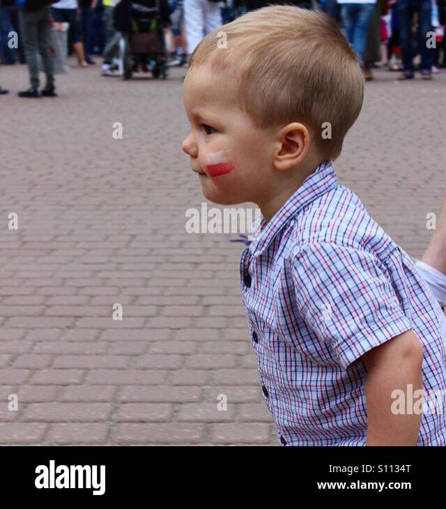 Un profil de baby boy en mouvement portant chemise manches courtes, étant à l'extérieur, avec le drapeau national polonais peint sur sa joue Banque D'Images