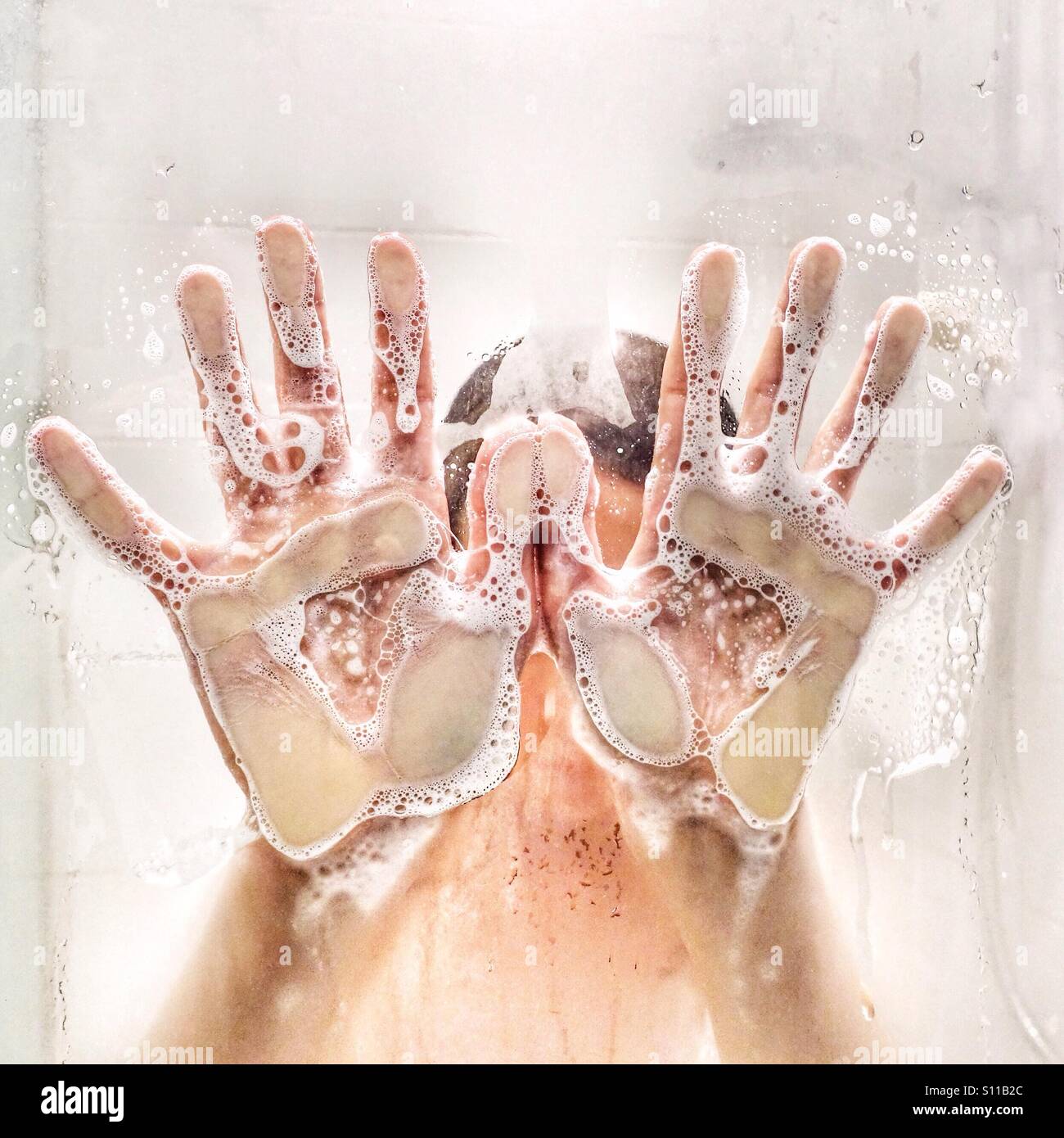 L'enfant mains savonneuse pressé contre la porte de la douche Banque D'Images