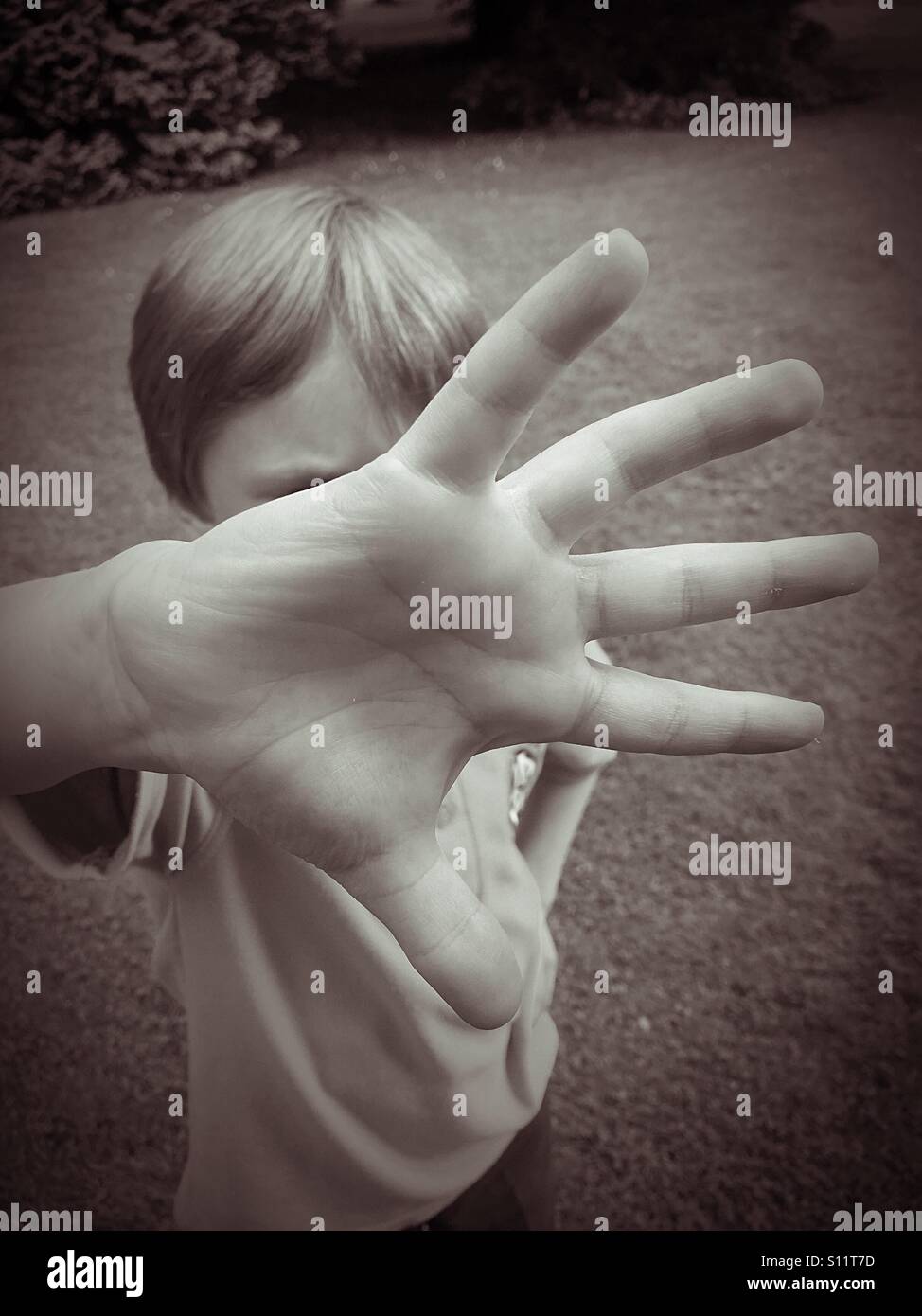 Une image pour illustrer les questions sociales de l'enfant. Un garçon de six ans couvre son visage en étalant ses doigts et en poussant sa main vers l'appareil photo. Crédits photos - © COLIN HOSKINS. Banque D'Images