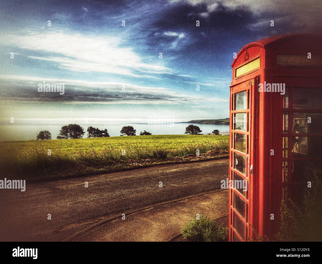 Image stylisée de la cabine téléphonique rouge britannique surplombant Lunan Bay sur la côte est de l'Écosse, avec un ciel spectaculaire et un paysage côtier rural. - Image de stock capturée avec un smartphone
