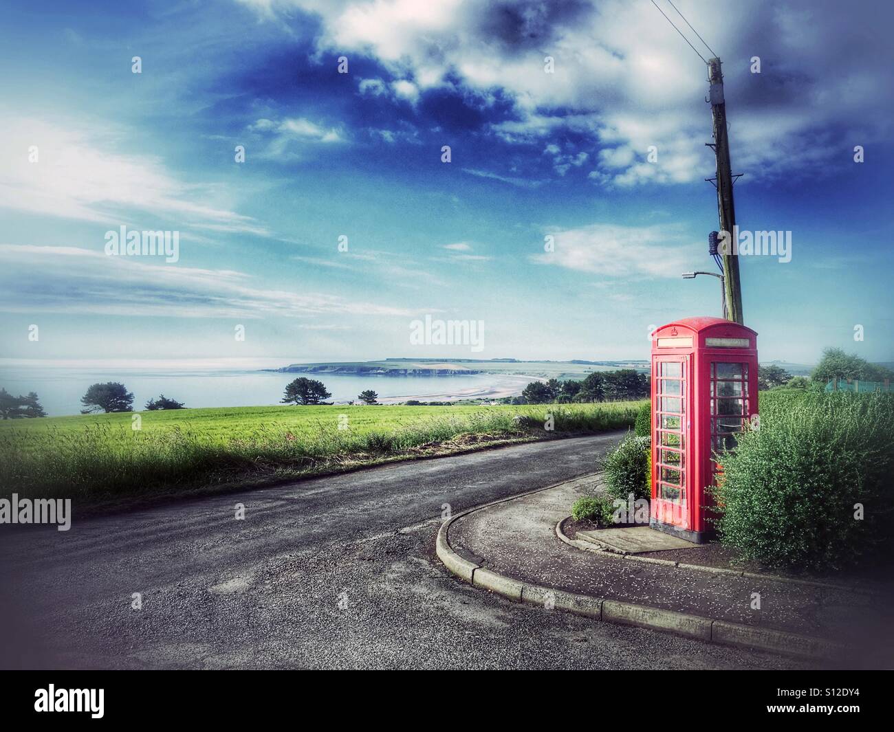 Cabine téléphonique rouge britannique à côté d'une route rurale surplombant Lunan Bay sur la côte est de l'Écosse, avec un ciel spectaculaire et un paysage côtier. - Image de stock capturée avec un smartphone