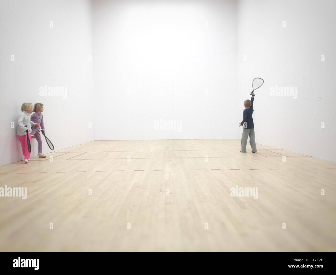 Trois enfants jouent un jeu improvisé de racquetball. Banque D'Images