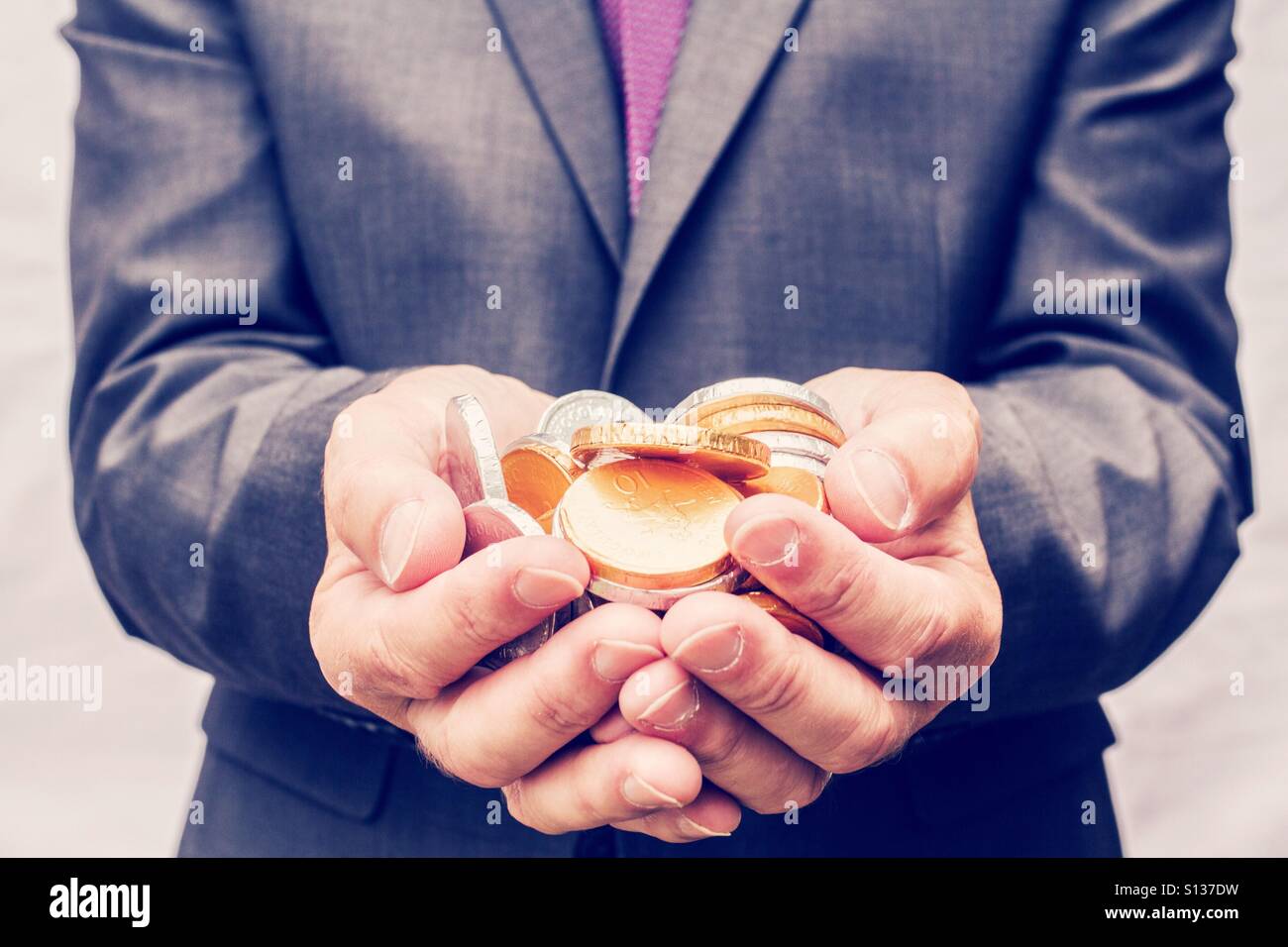 Un homme en costume tenant une poignée de pièces d'or et d'argent dans son creux des mains. Banque D'Images