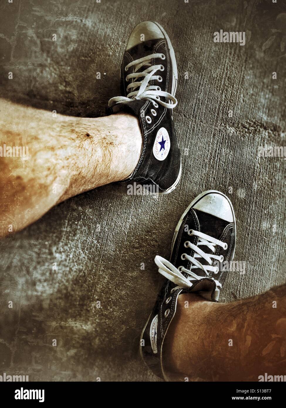 Les jambes poilues d'homme avec une paire de Converse chaussures de tennis Banque D'Images