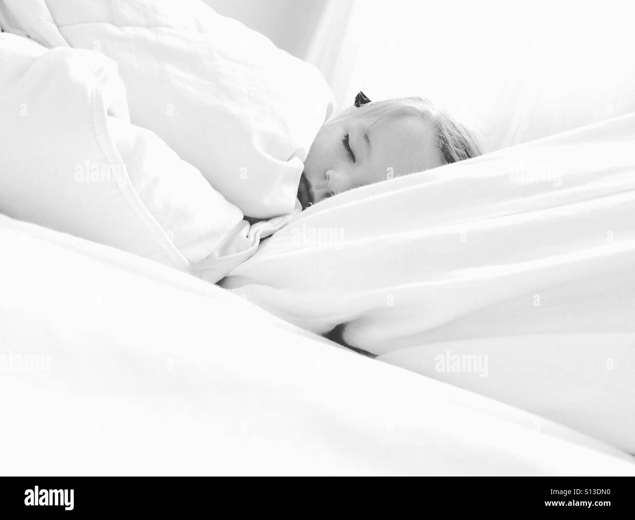 Enfant endormi dans un grand lit blanc Banque D'Images