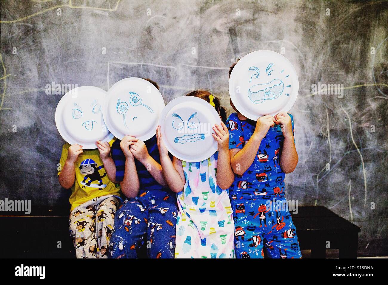 Quatre enfants en espérant les assiettes de papier avec des visages émotionnels tirés en eux Banque D'Images