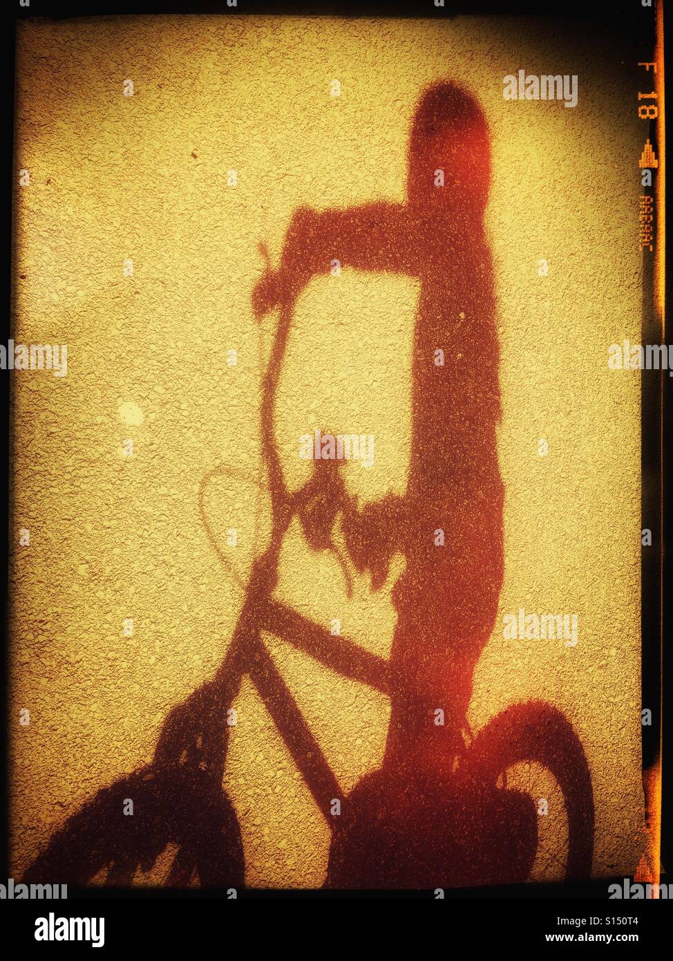 Une ombre rouge d'un enfant à cheval un petit vélo. L'ombre est sur une surface goudronnée (asphalte). Crédits photos - © COLIN HOSKINS. Banque D'Images
