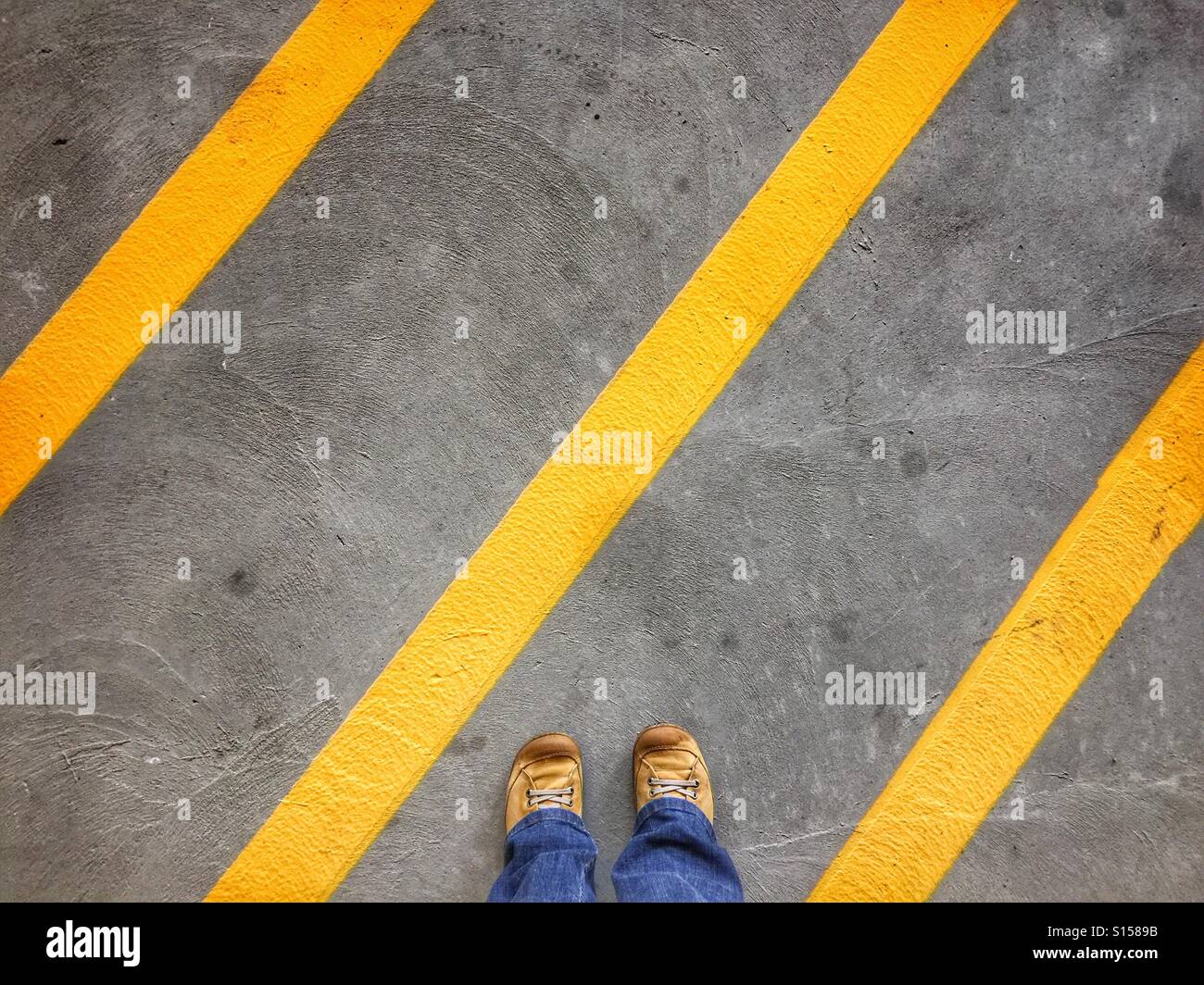 Chaussures jaune sale figurent parmi la diagonale jaune indiquant l'absence d'une zone de stationnement stationnement en béton. Banque D'Images