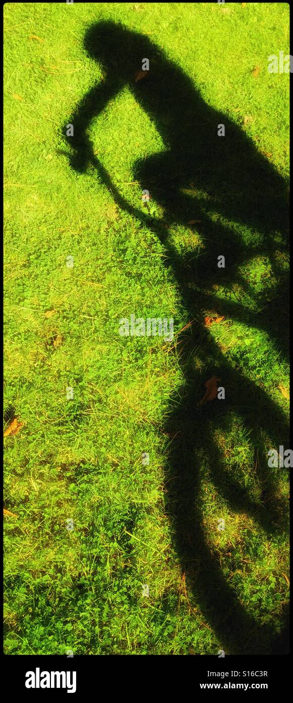 L'ombre d'un enfant avec un vélo. C'est l'été, l'herbe est verte et le soleil brille. L'enfance est super ! Crédits photos - © COLIN HOSKINS. Banque D'Images