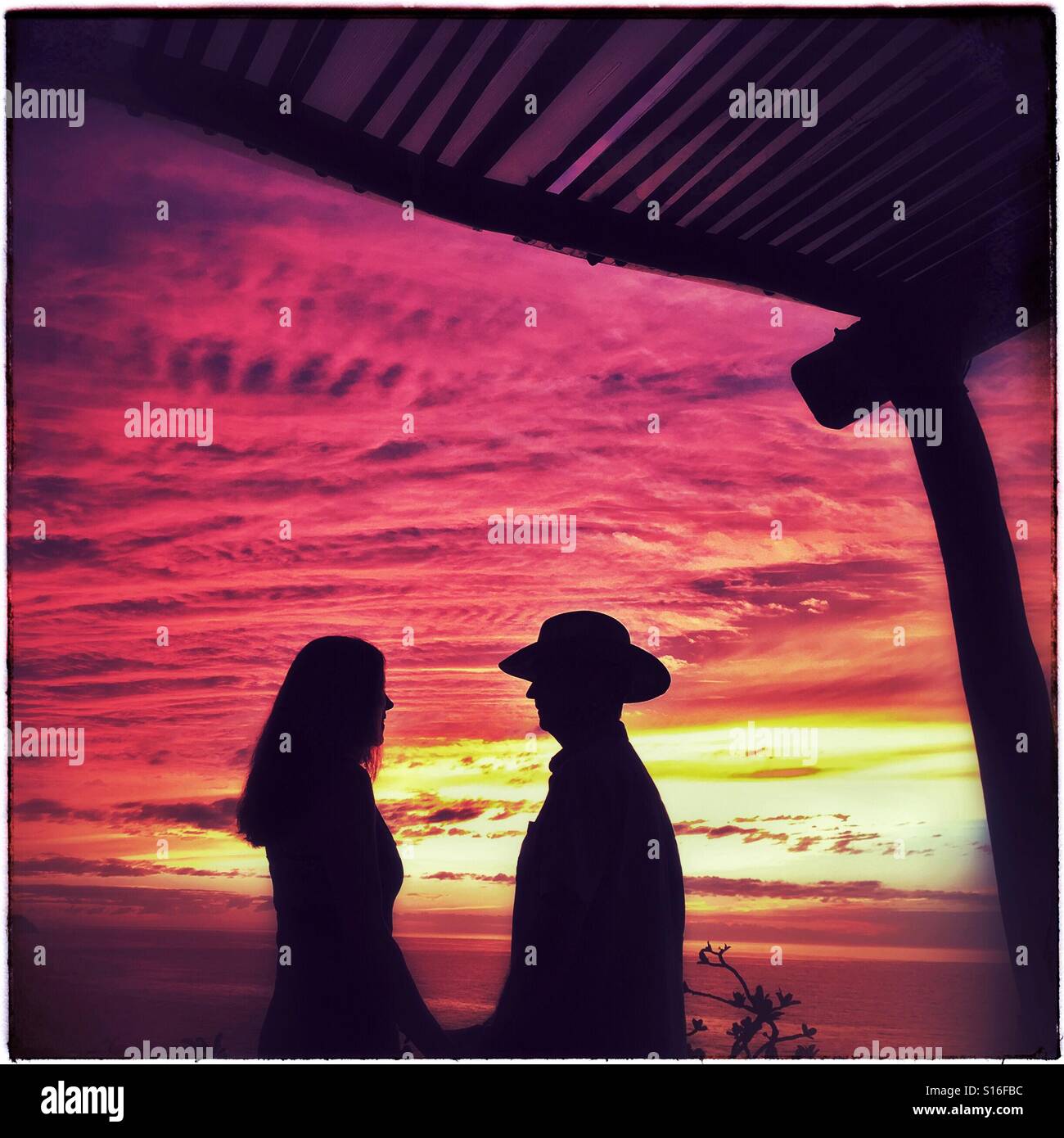Un couple hétérosexuel en silhouette bénéficie de la compagnie des autres et la vue d'un magnifique coucher du soleil. Banque D'Images
