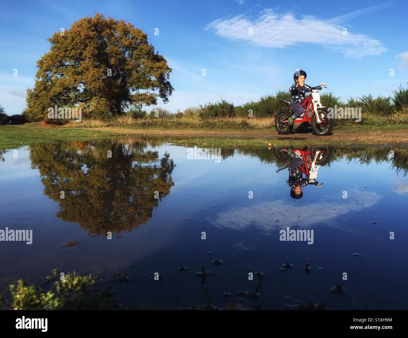 Un garçon de 9 ans un OSET manèges, une moto de trial fonctionnant sur batterie, passé une flaque sur la lande près de Hartley Wintney, Hampshire Novembre 2016 Banque D'Images