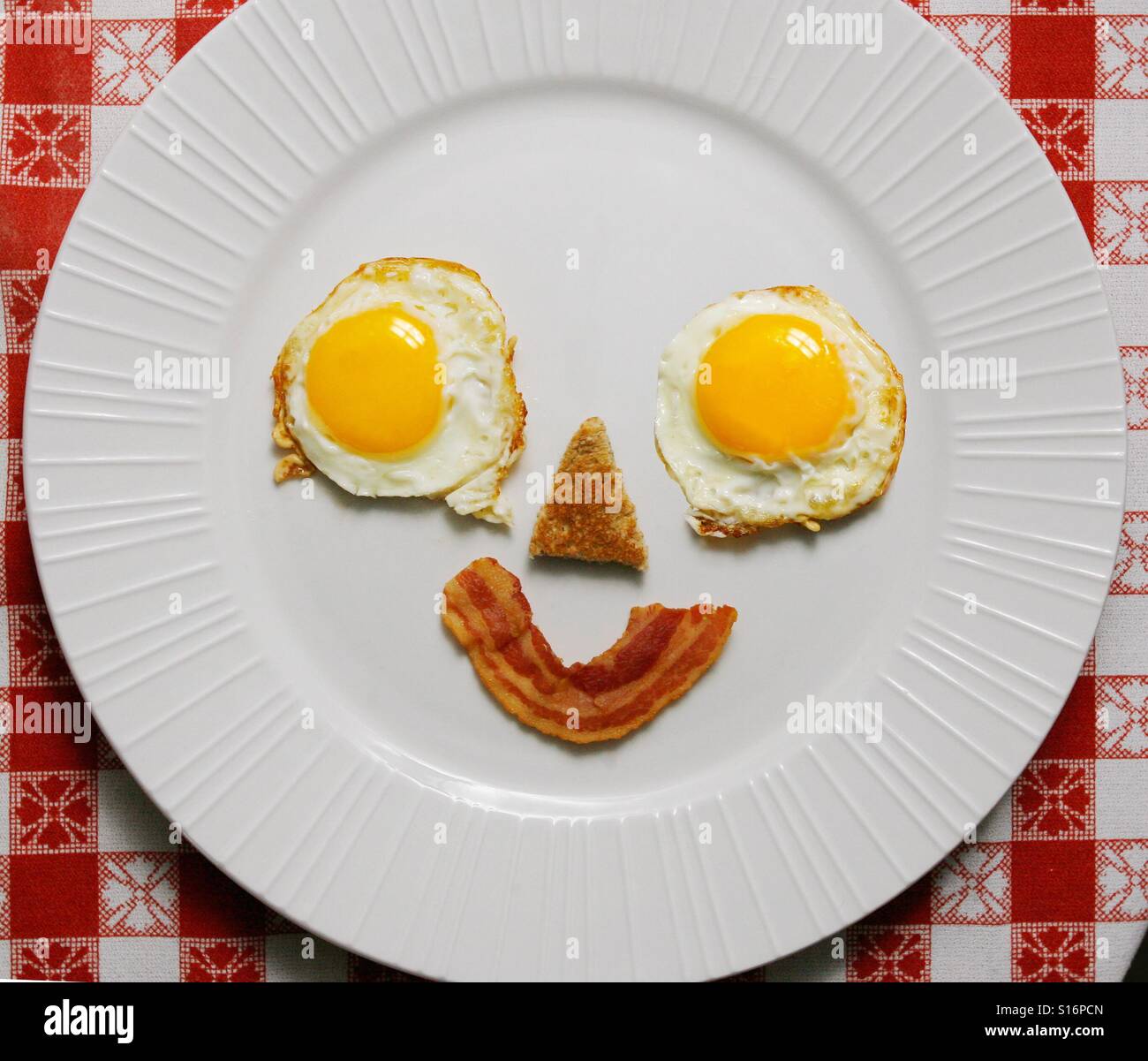 Deux œufs, un morceau de pain grillé et une tranche de bacon faire un visage souriant sur une assiette petit-déjeuner - Image de stock capturée avec un smartphone