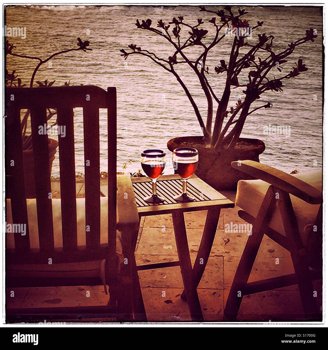 Deux verres de vin rouge dans des verres bleu soufflé à la mexicaine s'asseoir sur une table en teck chaises teck entre sur un pont dans le Nayarit, Mexique avec vue sur l'océan Pacifique. Banque D'Images
