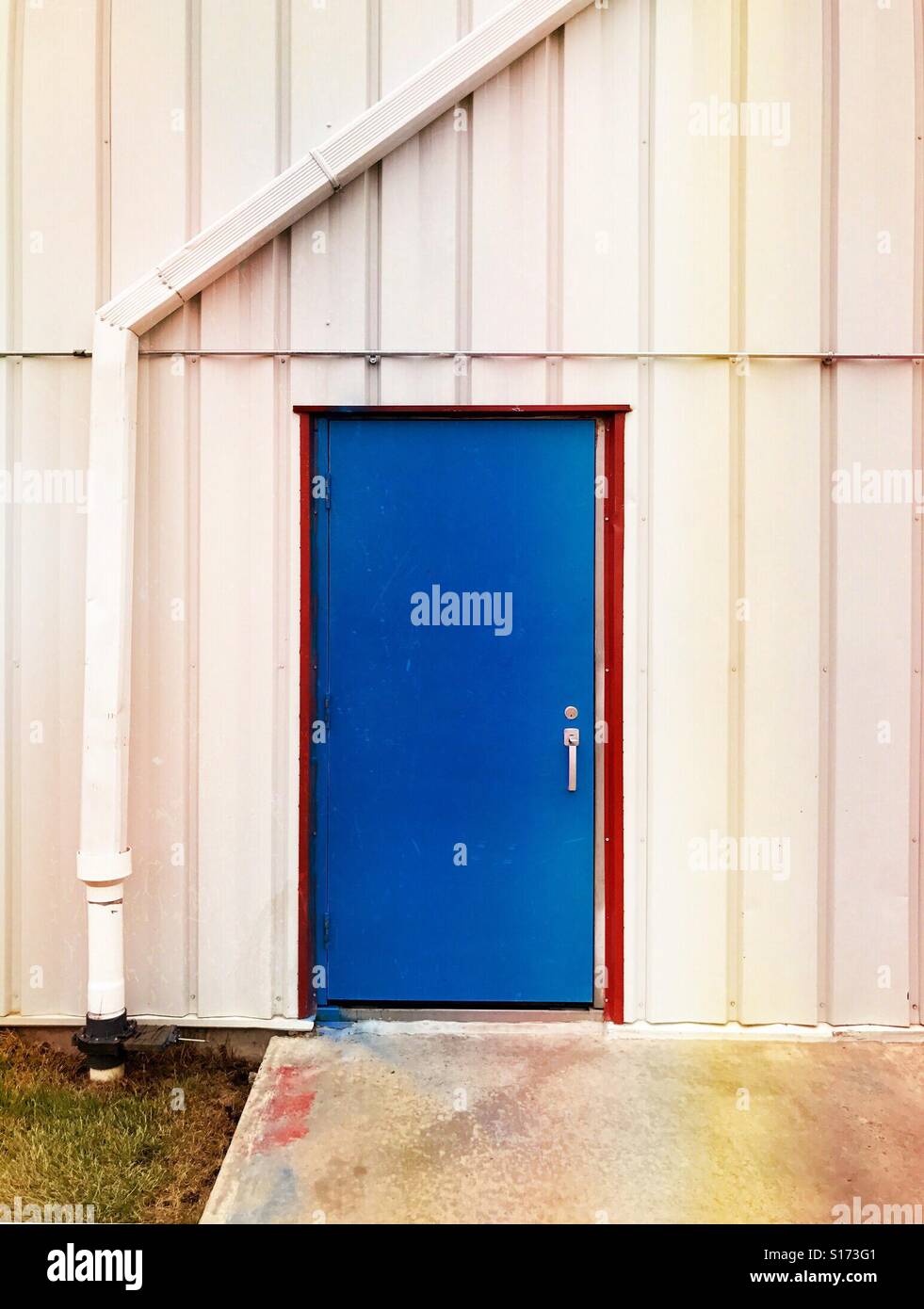 Une porte bleue avec un cadre rouge à travers un mur blanc. Banque D'Images