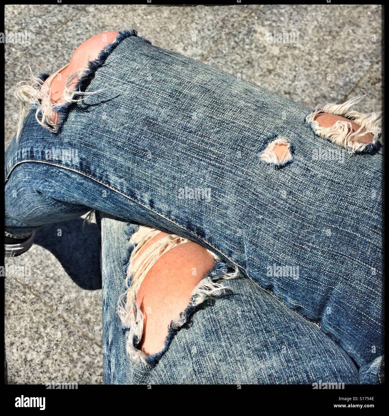 Jambes croisées portant un jean délavé et déchiré, USA, 2016, © Katharine Andriotis Banque D'Images