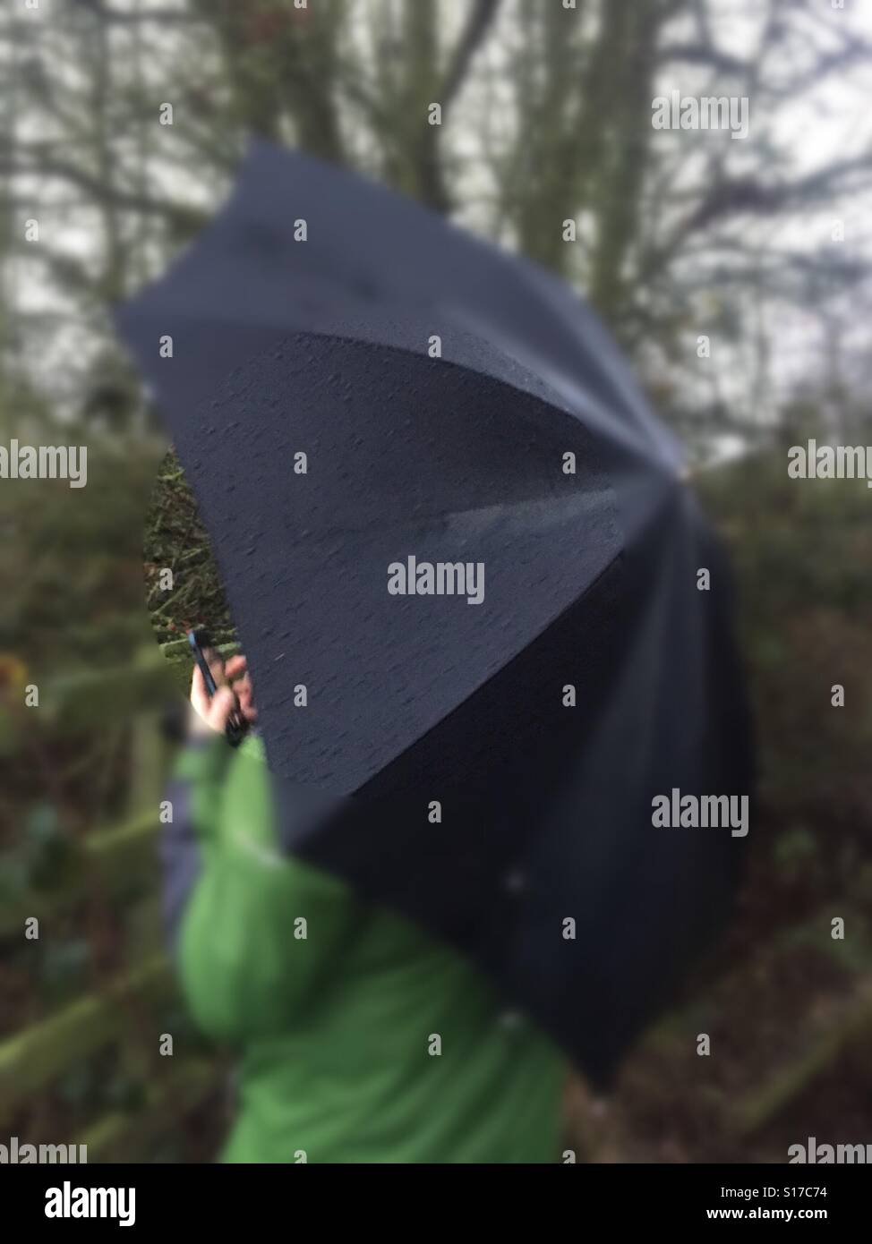 L'homme s'abritant sous parapluie noir à l'aide de mobile cell phone sous la pluie Banque D'Images