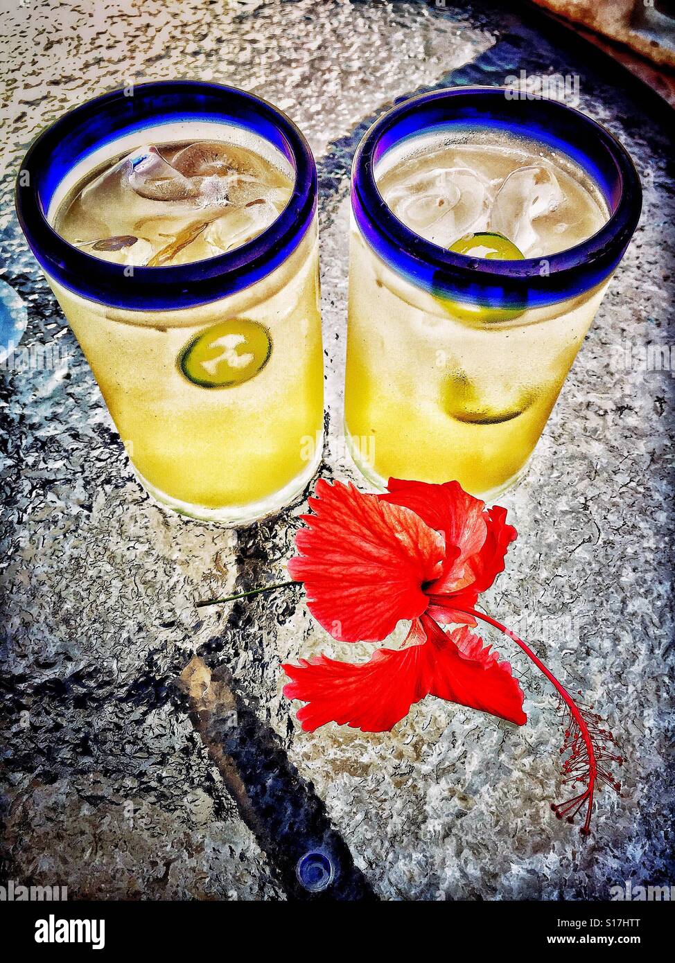 Lime rafraîchissante, pamplemousse et jalapeño spritz est servi dans main soufflée cerclée de bleu verres mexicains sur un patio extérieur table décorée d'une fleur d'hibiscus rouge. Banque D'Images