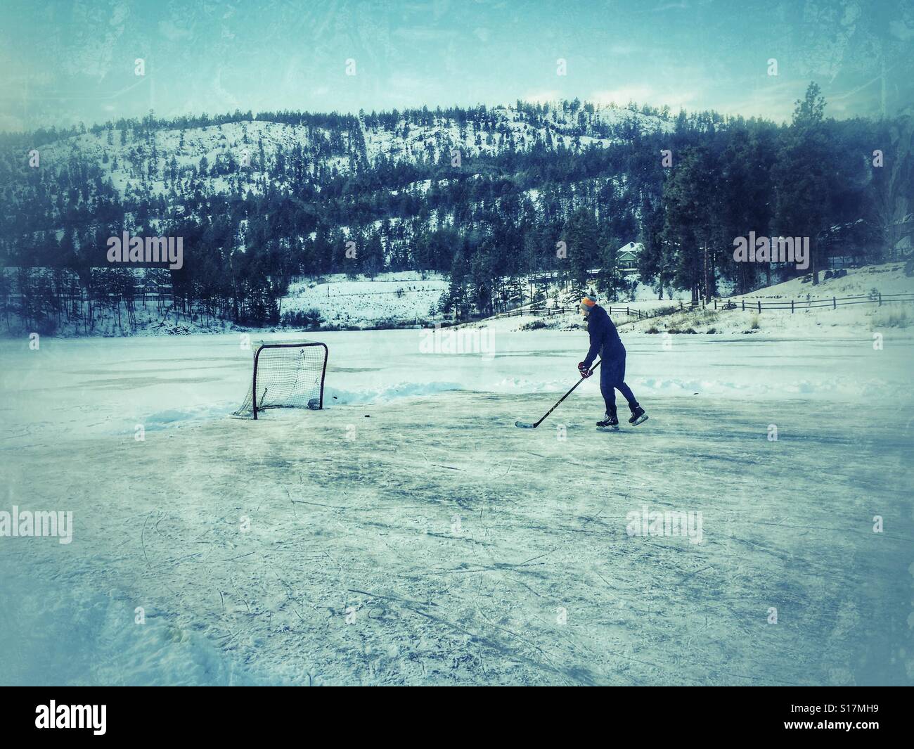 Jeune homme jouant au hockey sur étang une journée d'hiver à l'extérieur sur un lac gelé. Éditer en détresse. - Image de stock capturée avec un smartphone