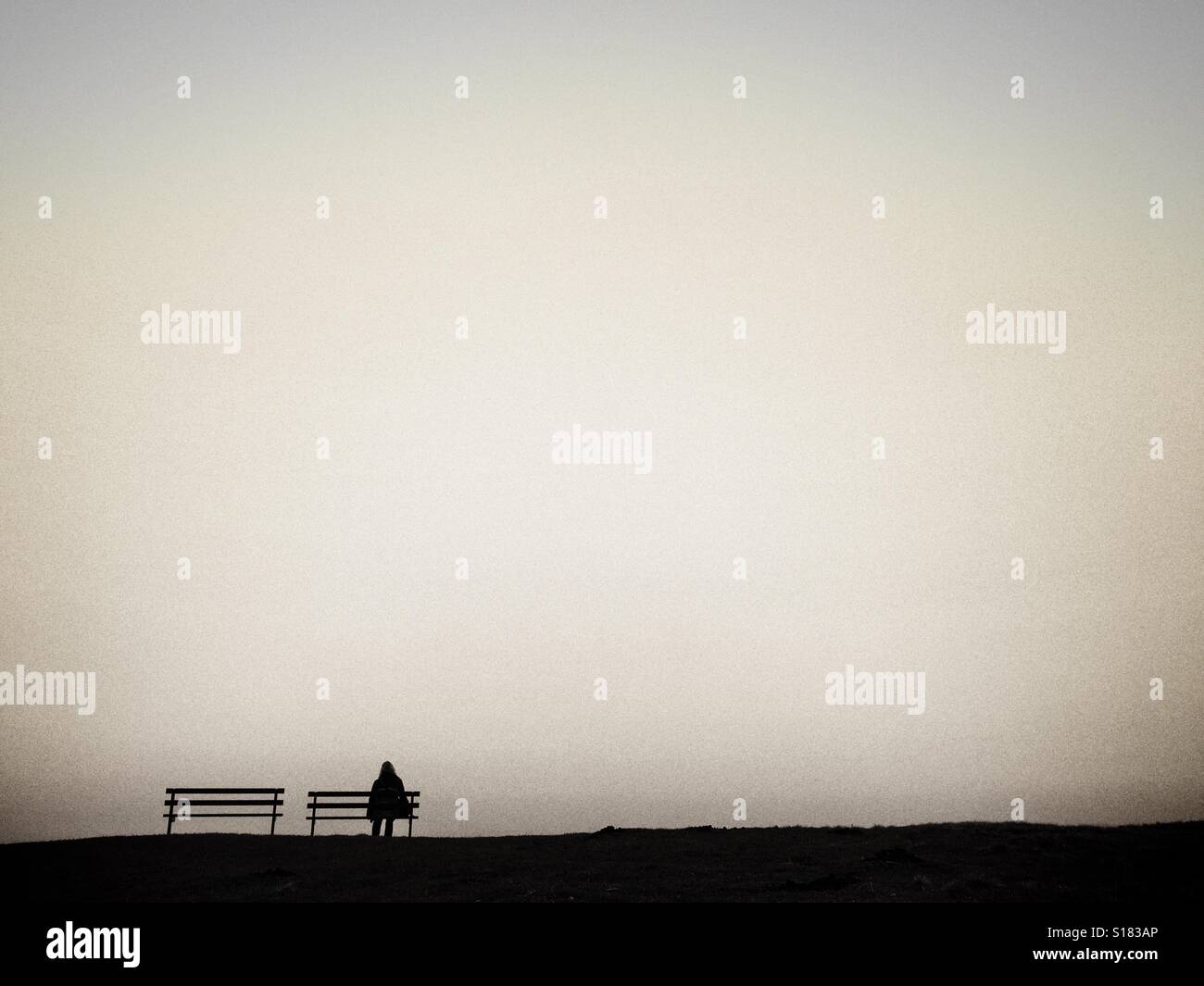 La figure solitaire sur un banc en silhouette contre un ciel clair Banque D'Images
