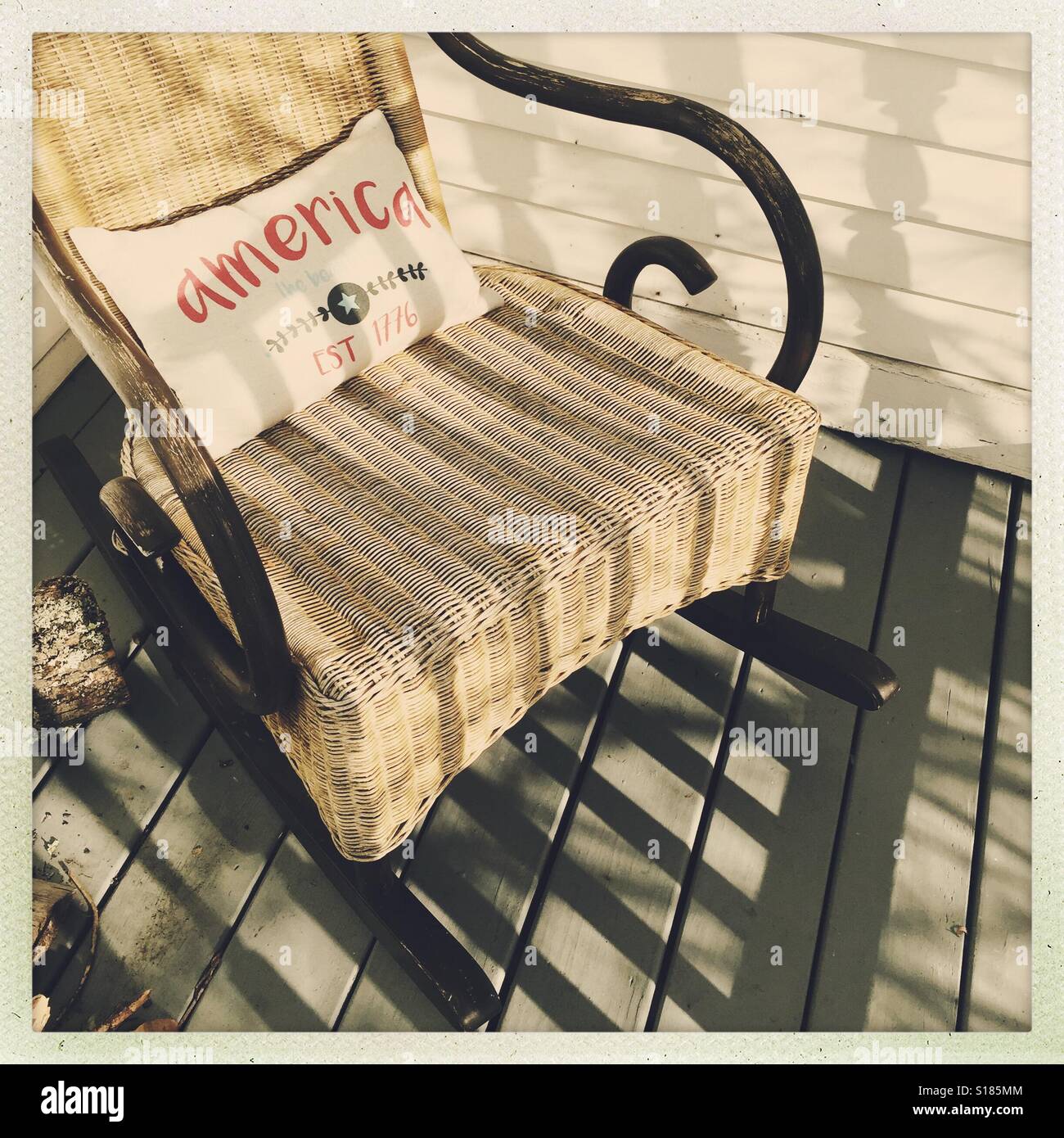Ombres sur une chaise à bascule vintage avec un oreiller patriotique, sur une véranda en bois. Banque D'Images