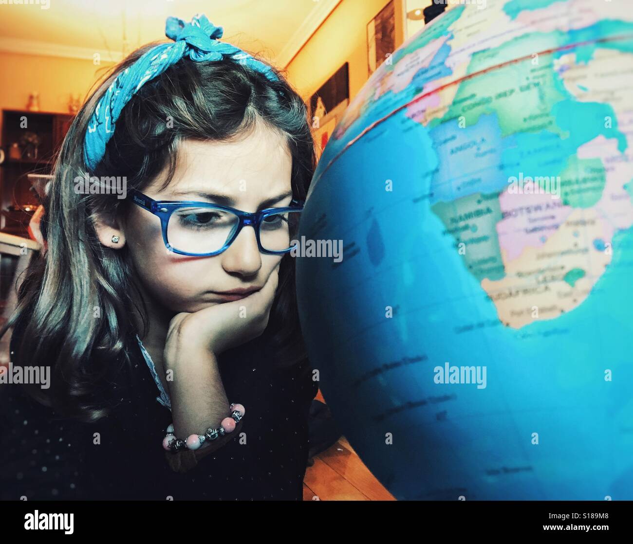 Petite fille avec des lunettes looking at a globe Banque D'Images