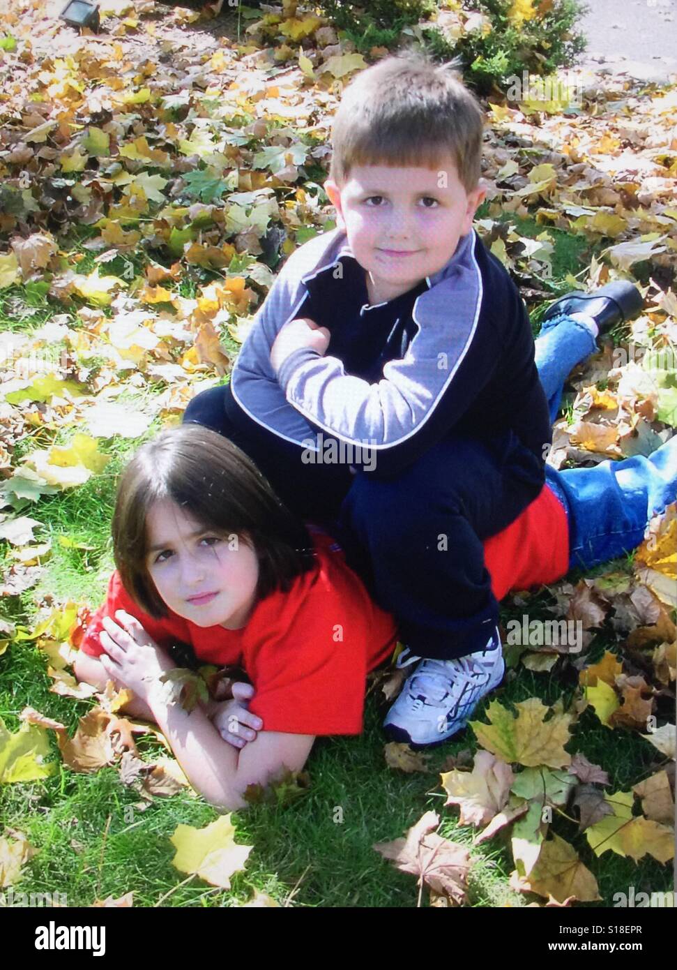 Un garçon assis sur le dessus d'une jeune fille au milieu des feuilles d'automne Banque D'Images