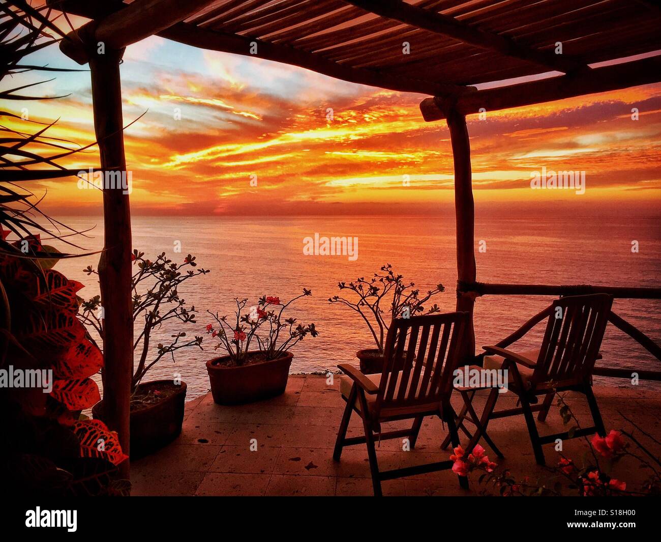 Vue sur un magnifique coucher de soleil sur l'océan Pacifique d'une terrasse avec chaises longues en teck dans le Nayarit, Mexique. Banque D'Images
