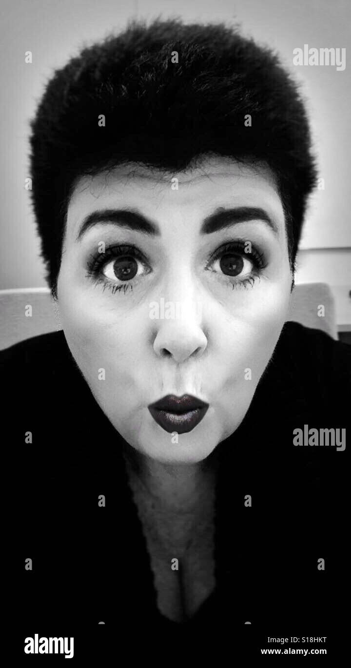 Un portrait en noir et blanc d'un dark haired woman Puckering ses lèvres et à la surprise Banque D'Images